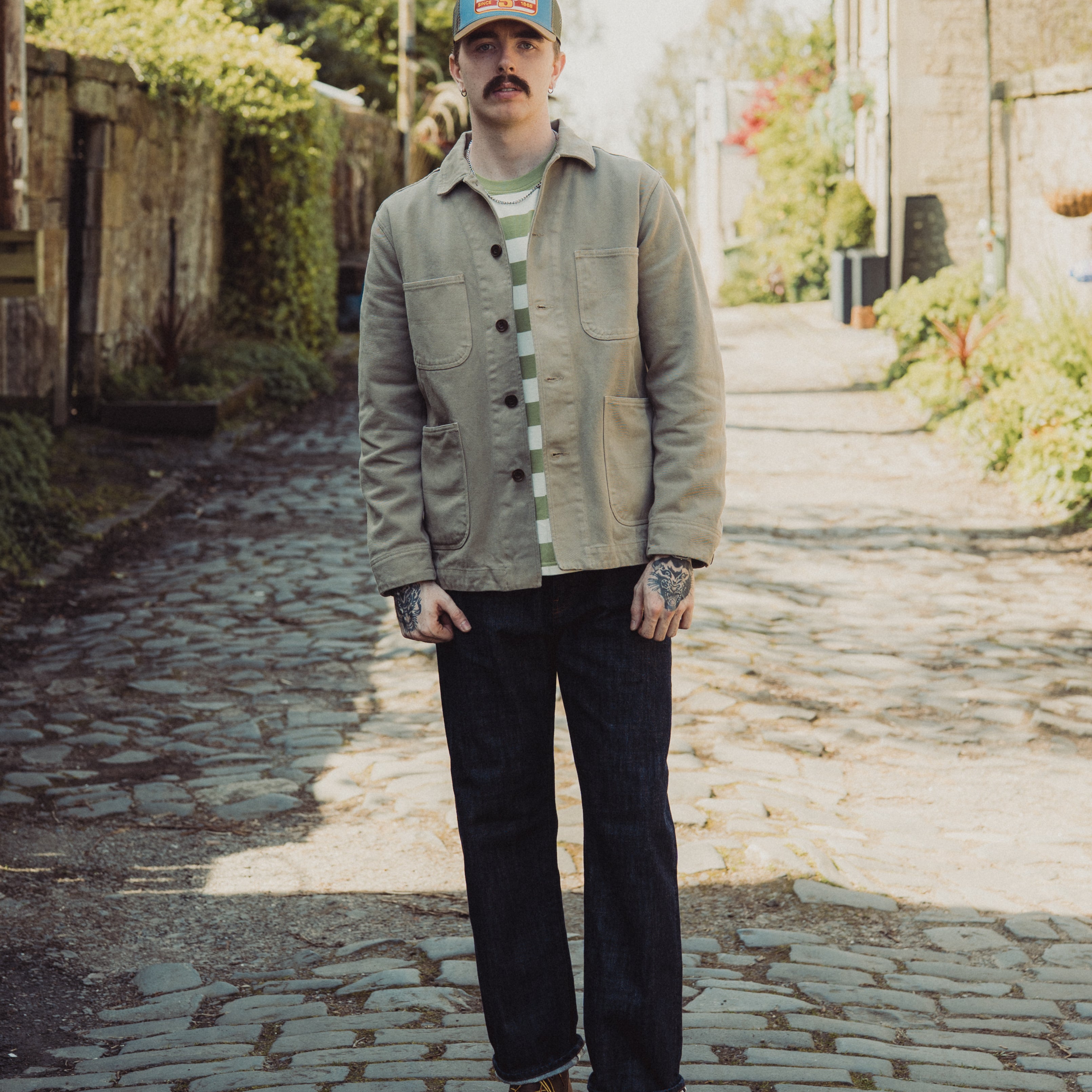 Man wearing a cap and jacket standing on a cobblestone street