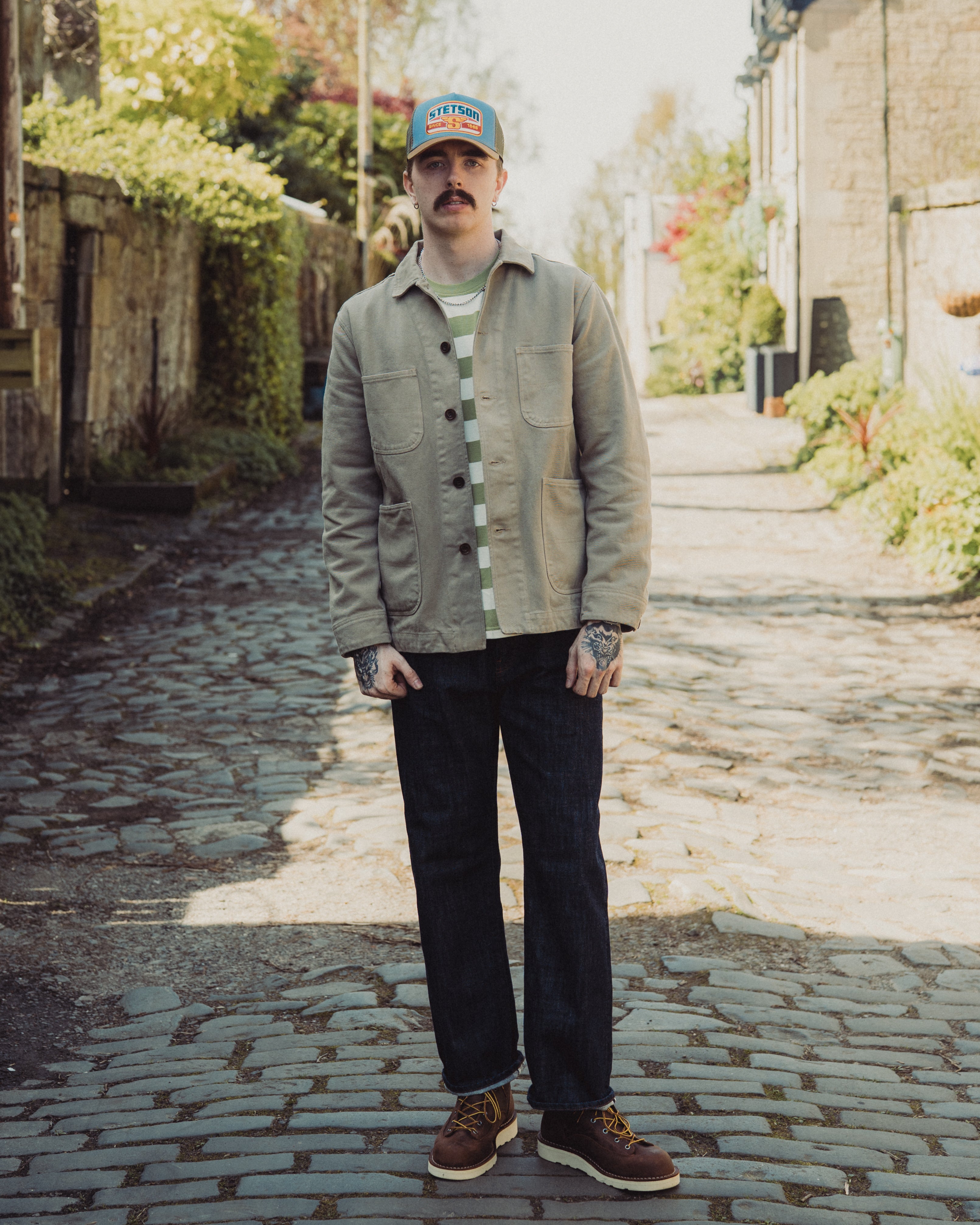 Man wearing a cap and jacket standing on a cobblestone street