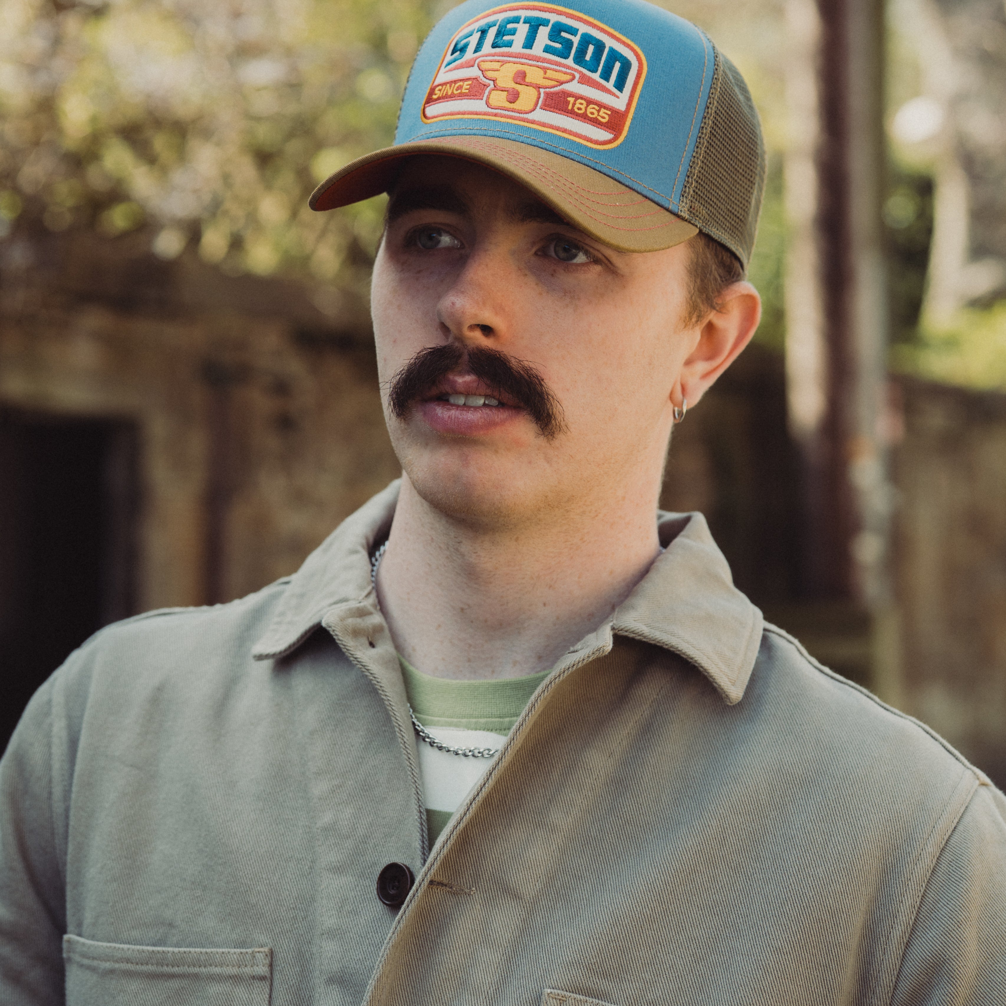 Man wearing a Stetson cap outdoors with a blurred natural background