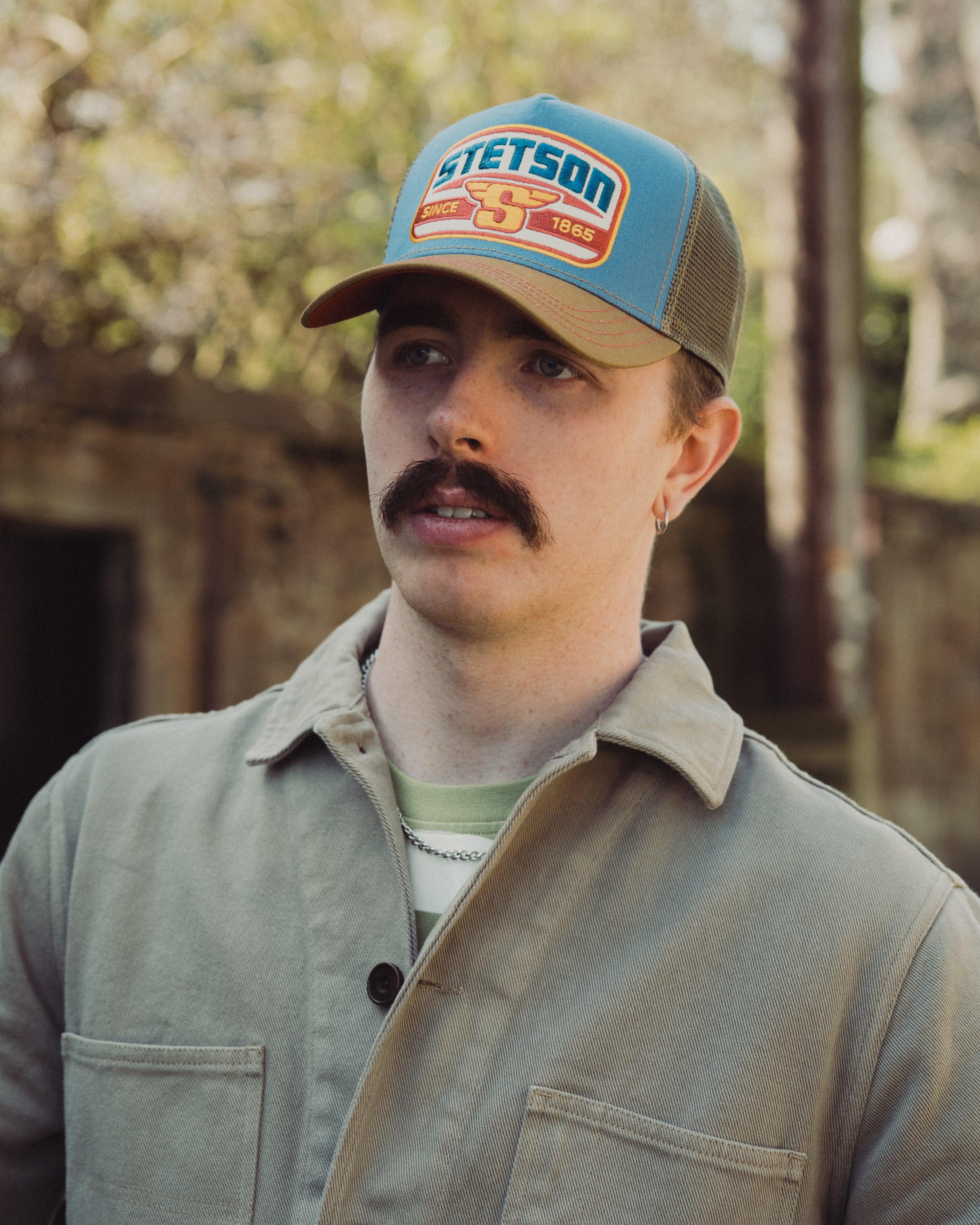 Man wearing a Stetson cap outdoors with a blurred natural background