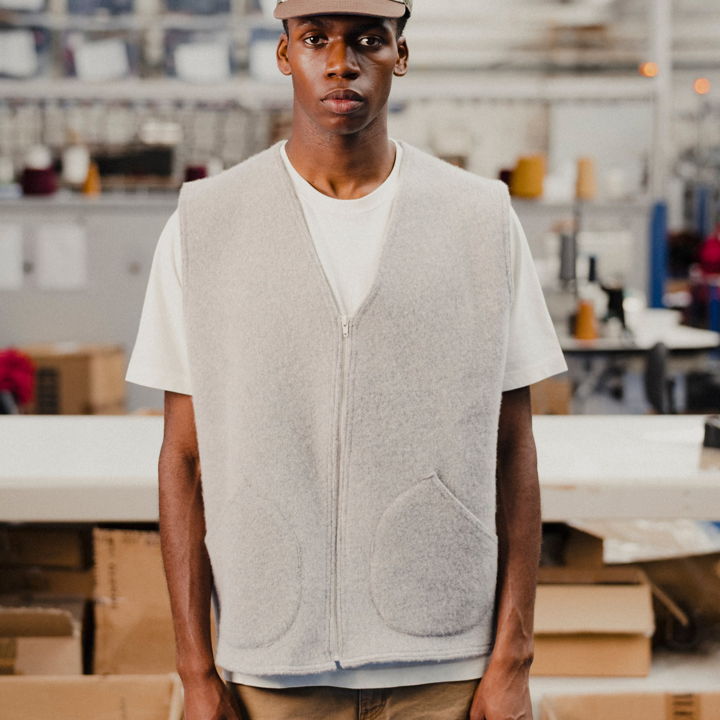 Man wearing a gray wool vest over a white t-shirt with a cap in an indoor setting
