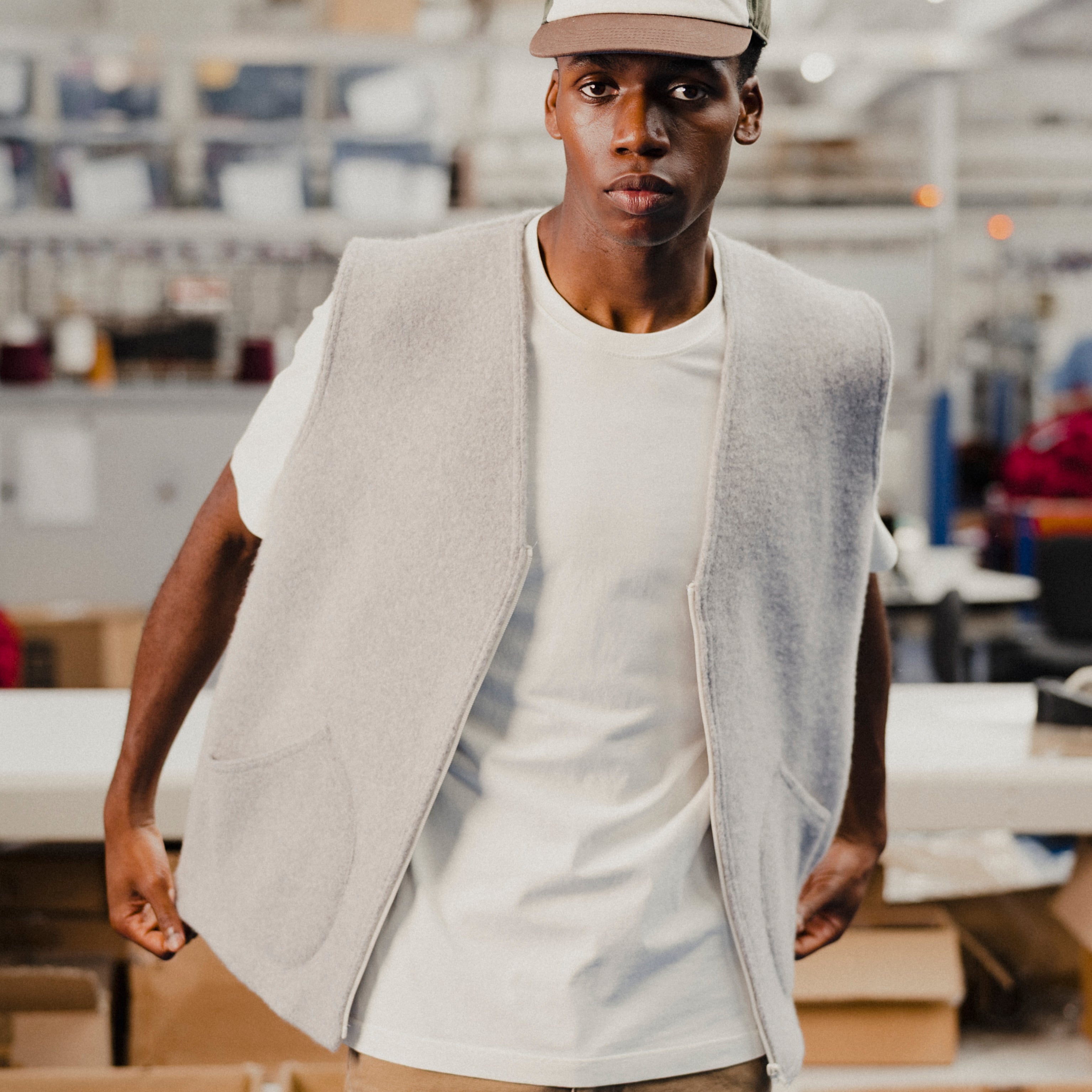 Man wearing a light gray wool vest over a white t-shirt with a cap in an indoor setting