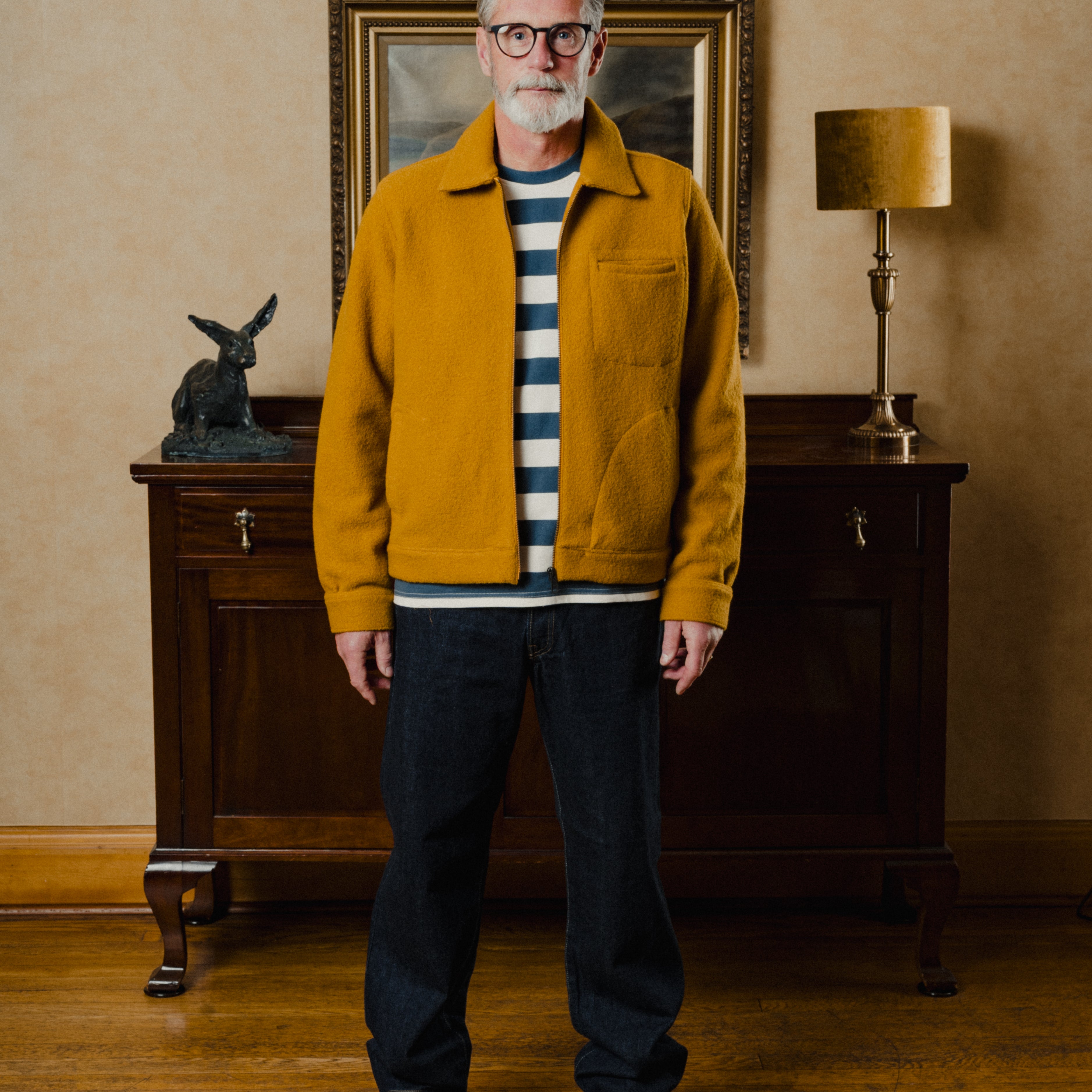 Man wearing a mustard jacket in an interior setting with a lamp and framed picture.