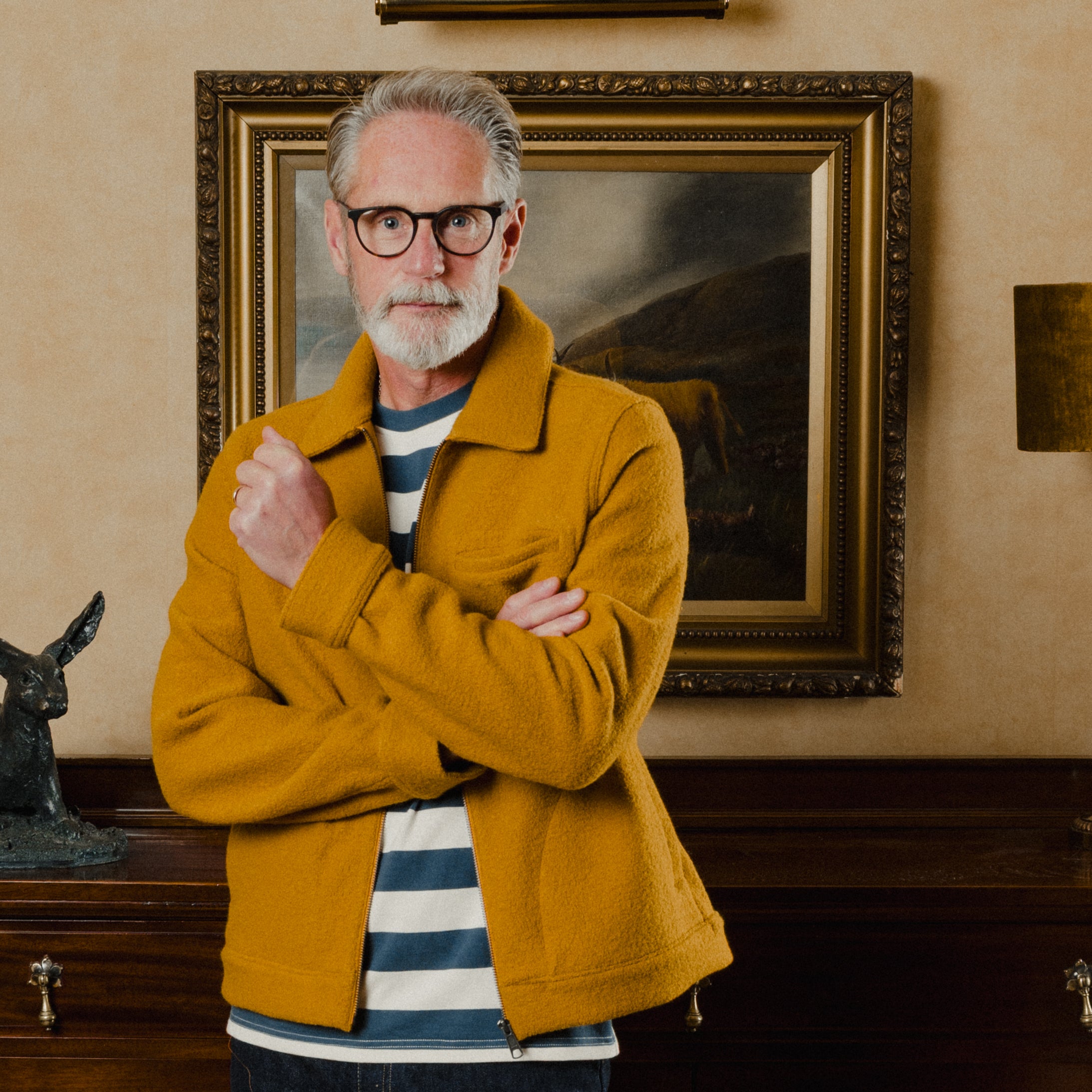 Man in a mustard jacket standing in a room with a painting on the wall