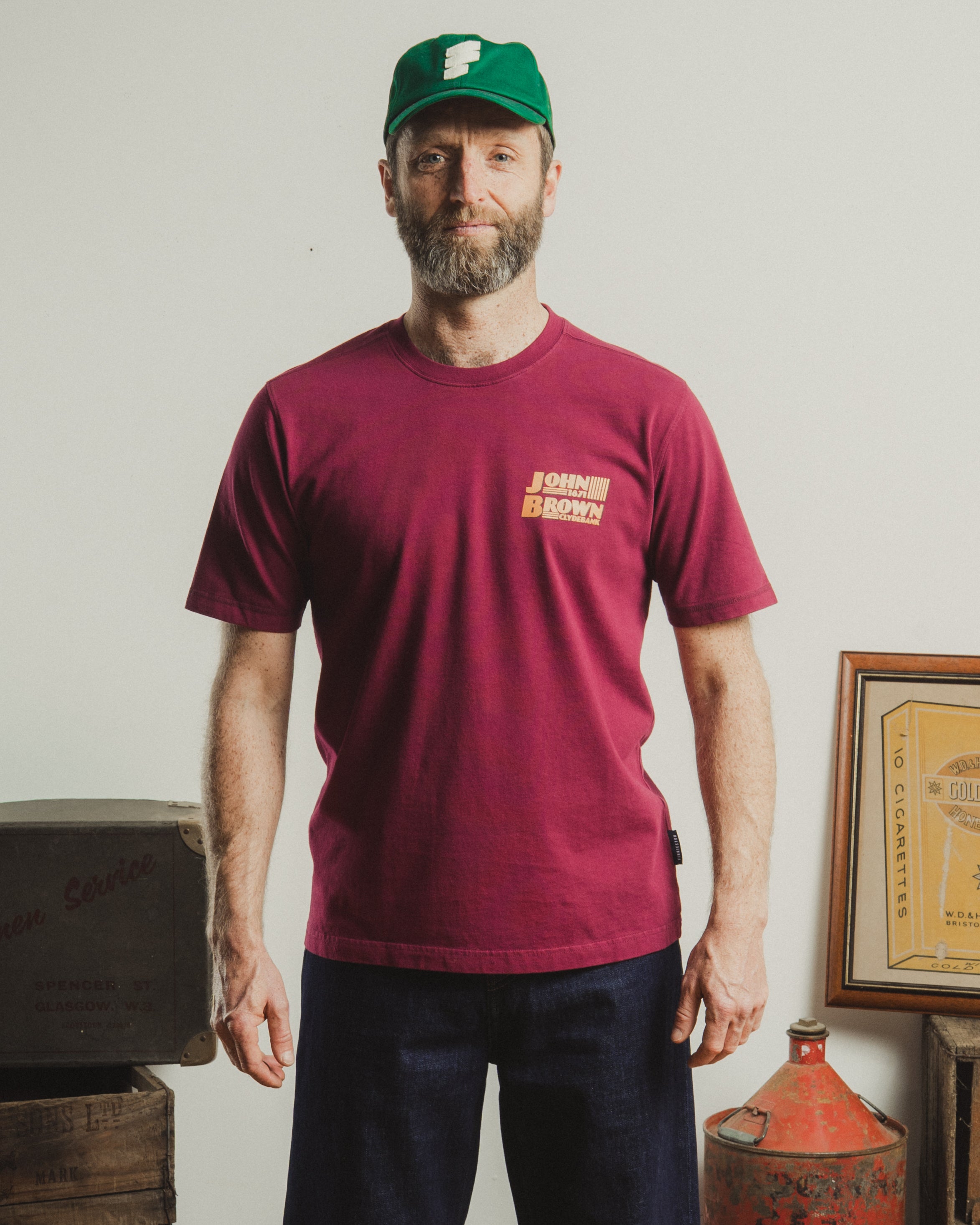 Man wearing a maroon t-shirt with text and a green cap indoors.