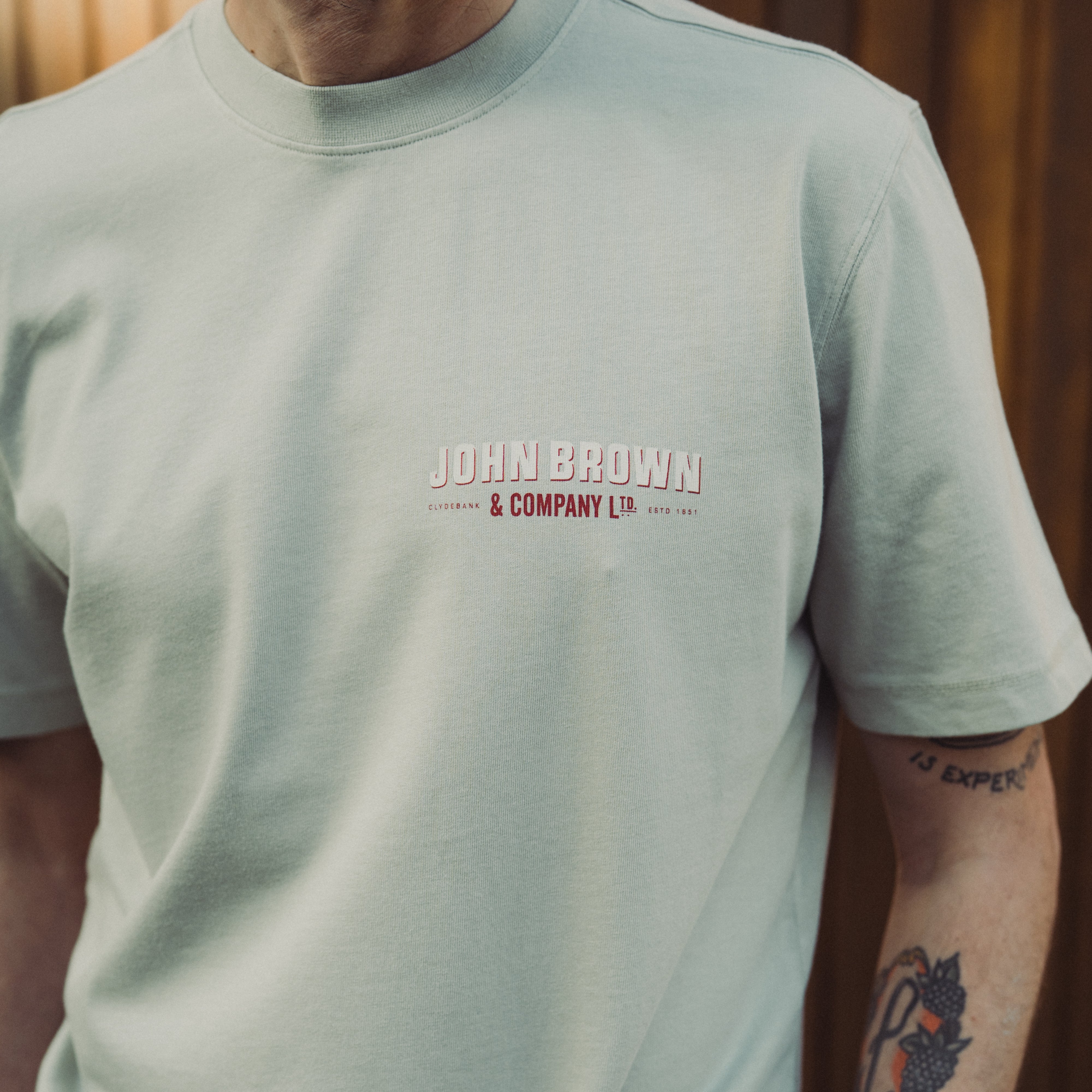 Person wearing a light green t-shirt with 'John Brown & Company Ltd' logo.