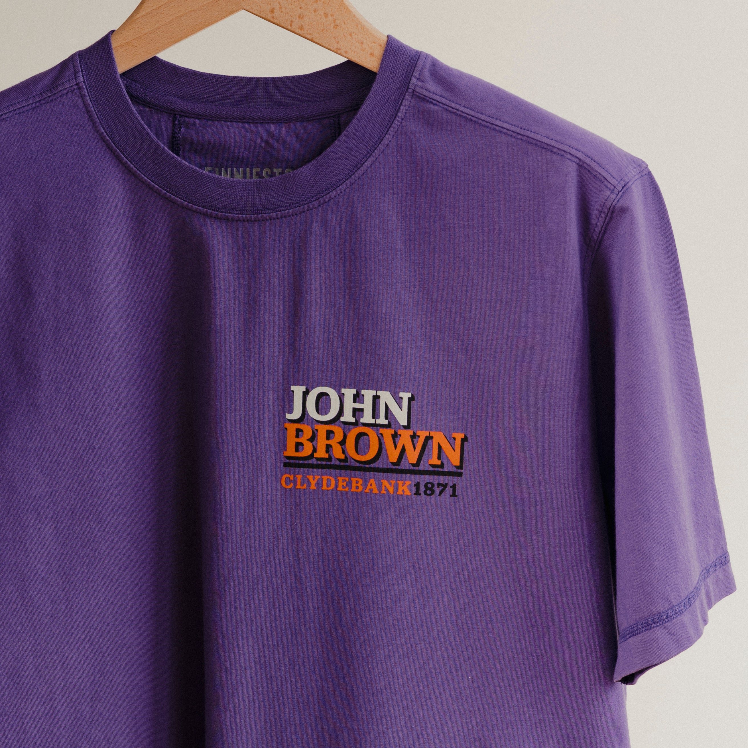 Purple t-shirt with 'John Brown Clydebank 1971' text on a hanger