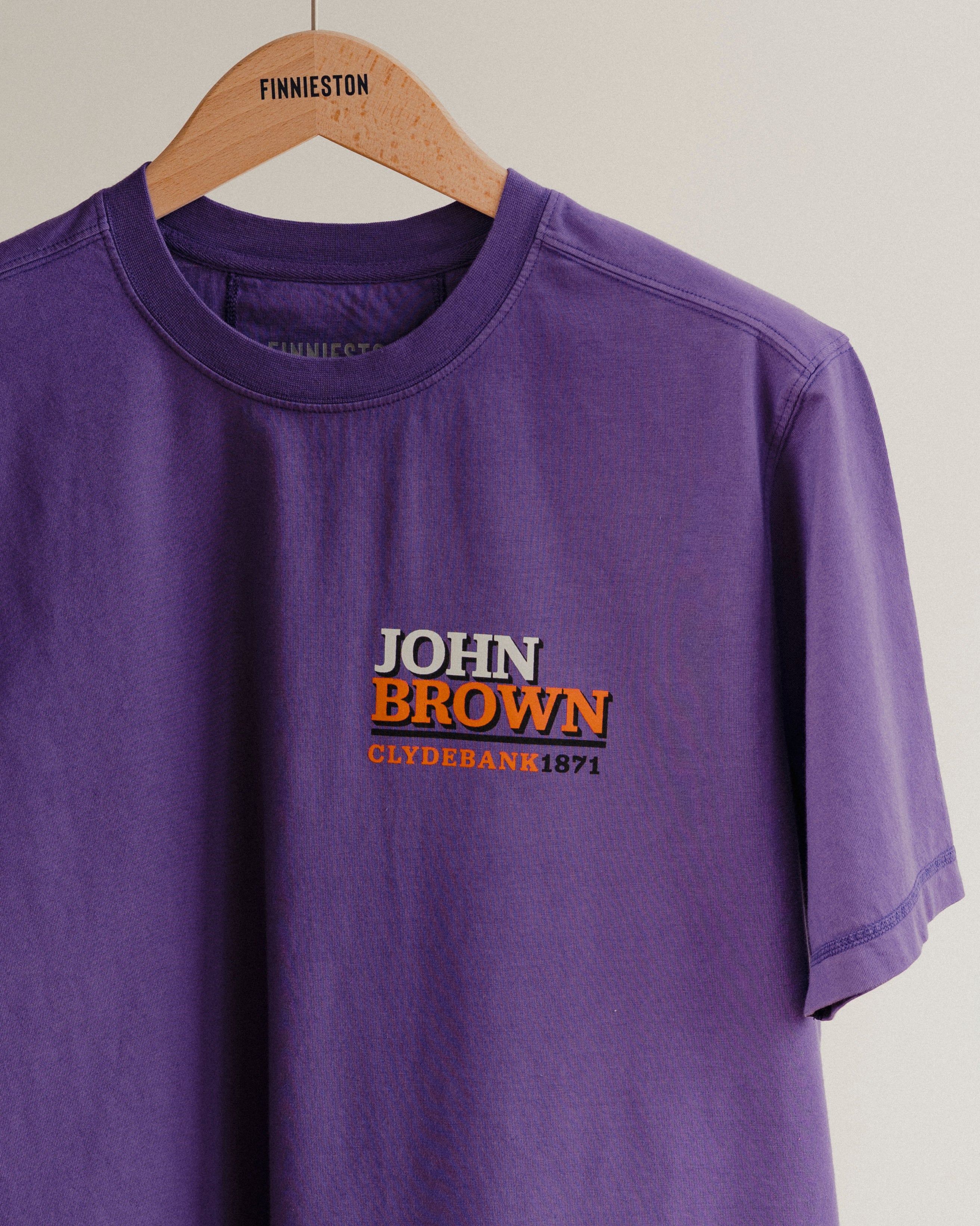Purple t-shirt with 'John Brown Clydebank 1971' text on a hanger
