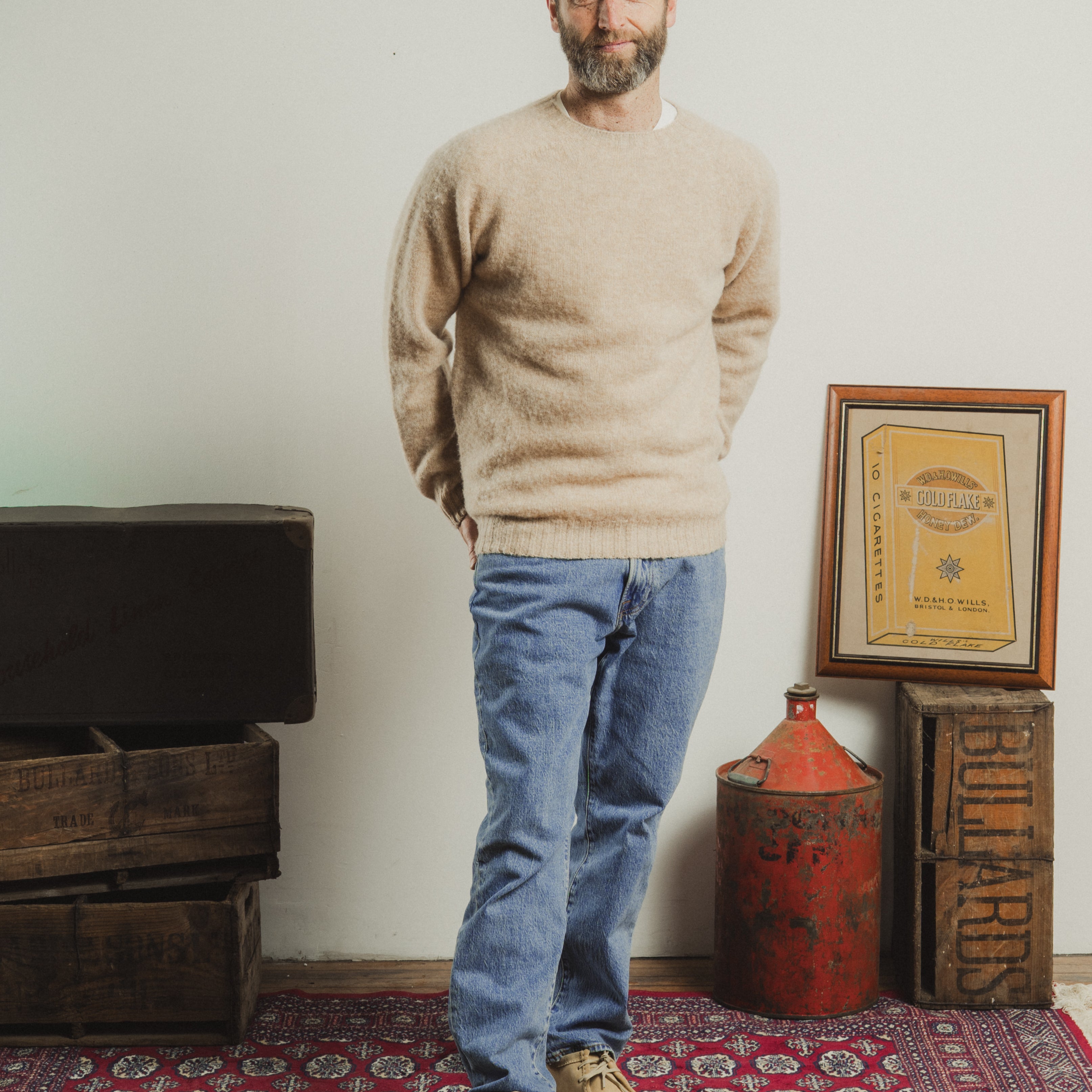 Man standing in a room with wooden crates and a framed document on the wall.