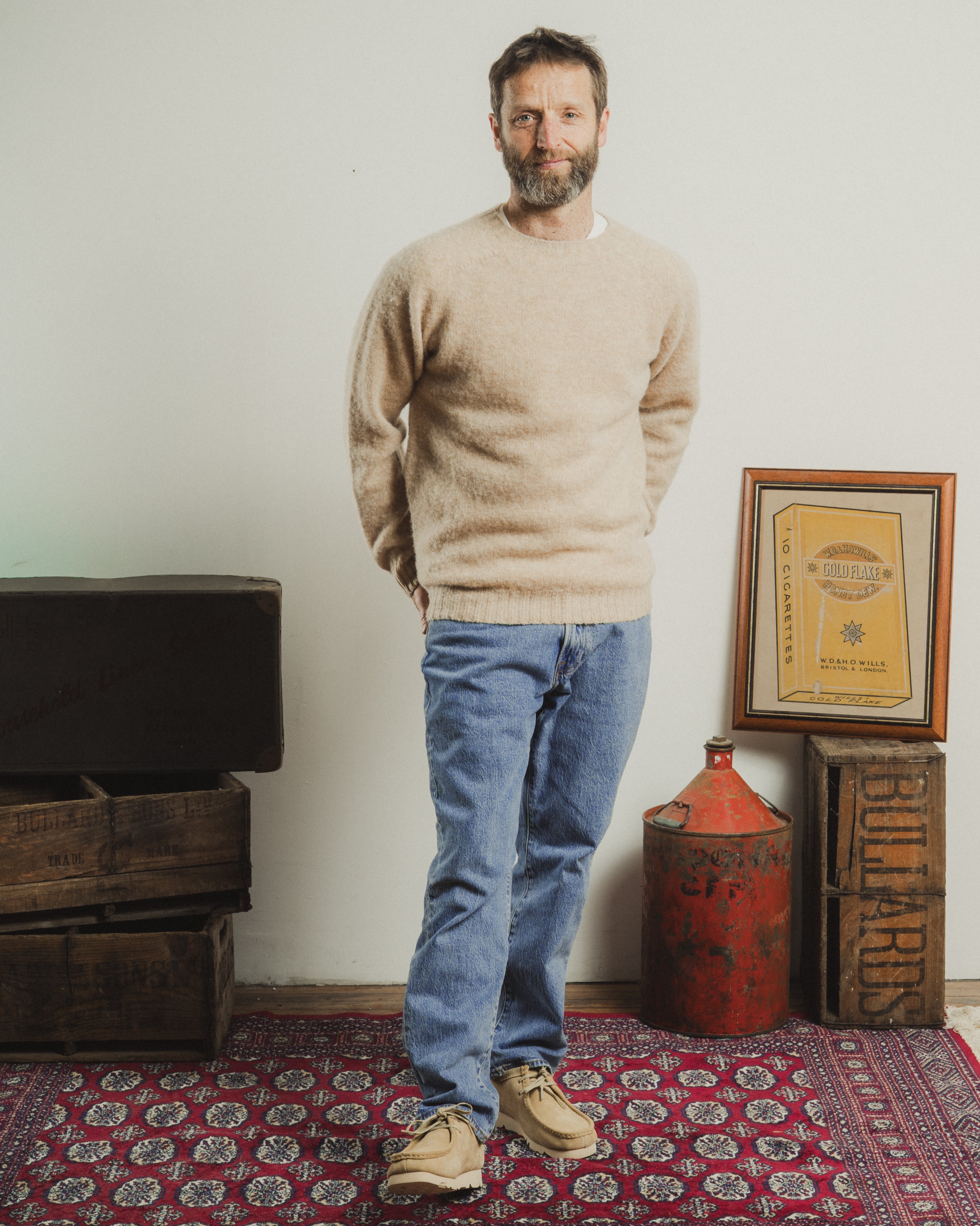 Man standing in a room with wooden crates and a framed document on the wall.