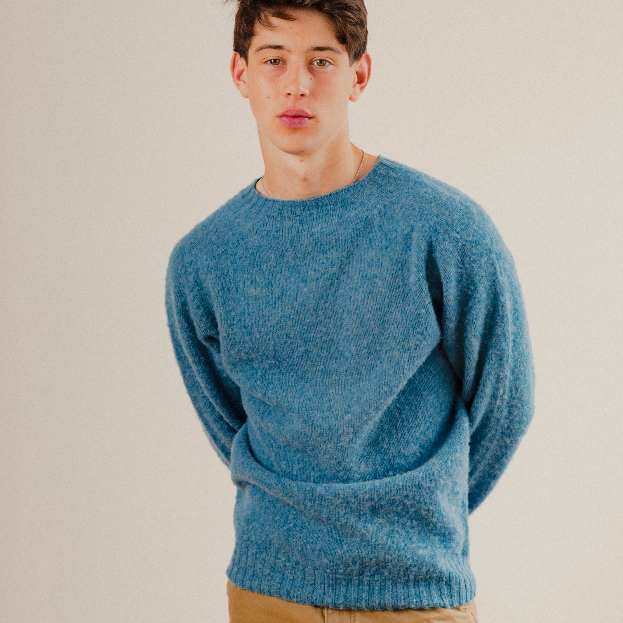 Man in a blue wool knit sweatshirt crewneck on a plain white background