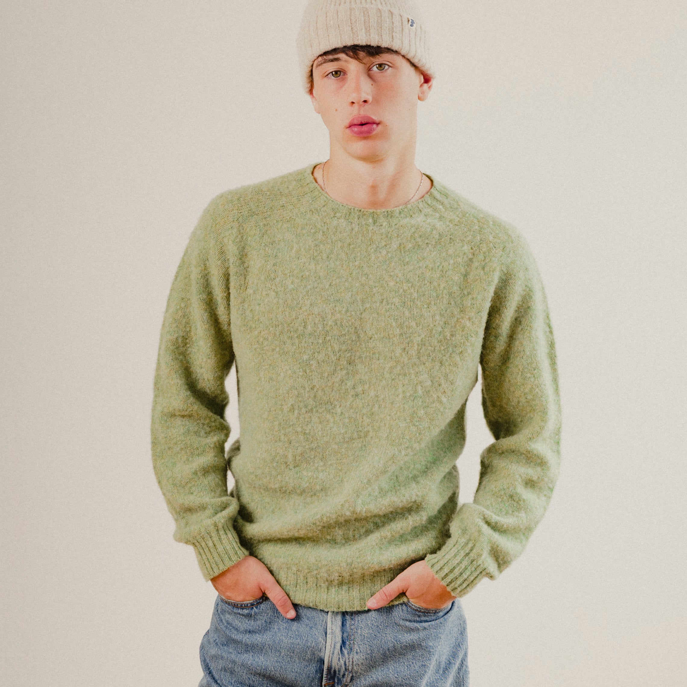 Person wearing a green wool knit sweater and beige beanie against a plain background
