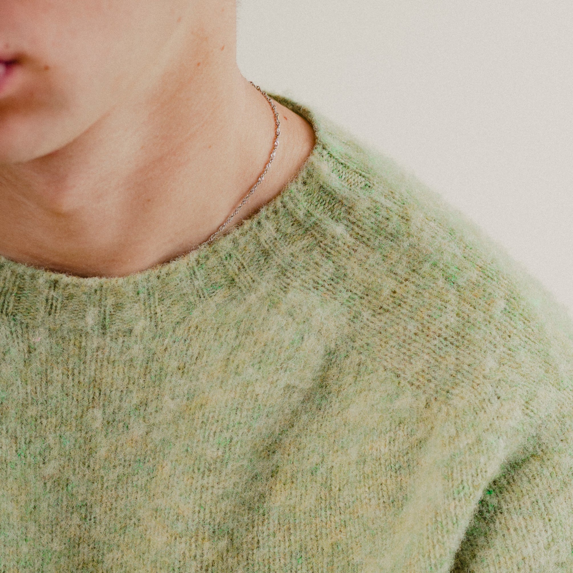 Close-up of a person wearing a green wool knitted sweater with a blurred background