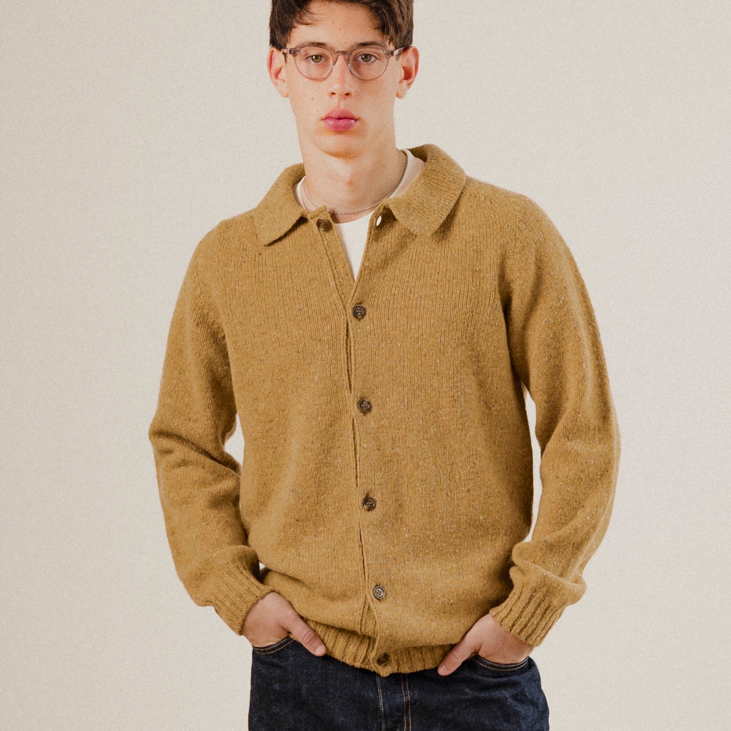 Man wearing a mustard yellow knitted wool cardigan against a plain background