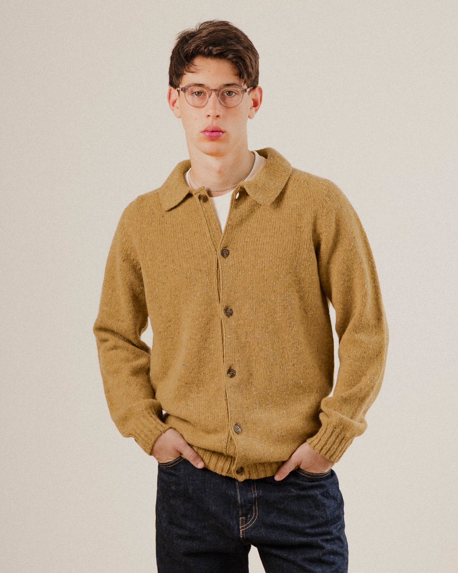 Man wearing a mustard yellow knitted wool cardigan against a plain background