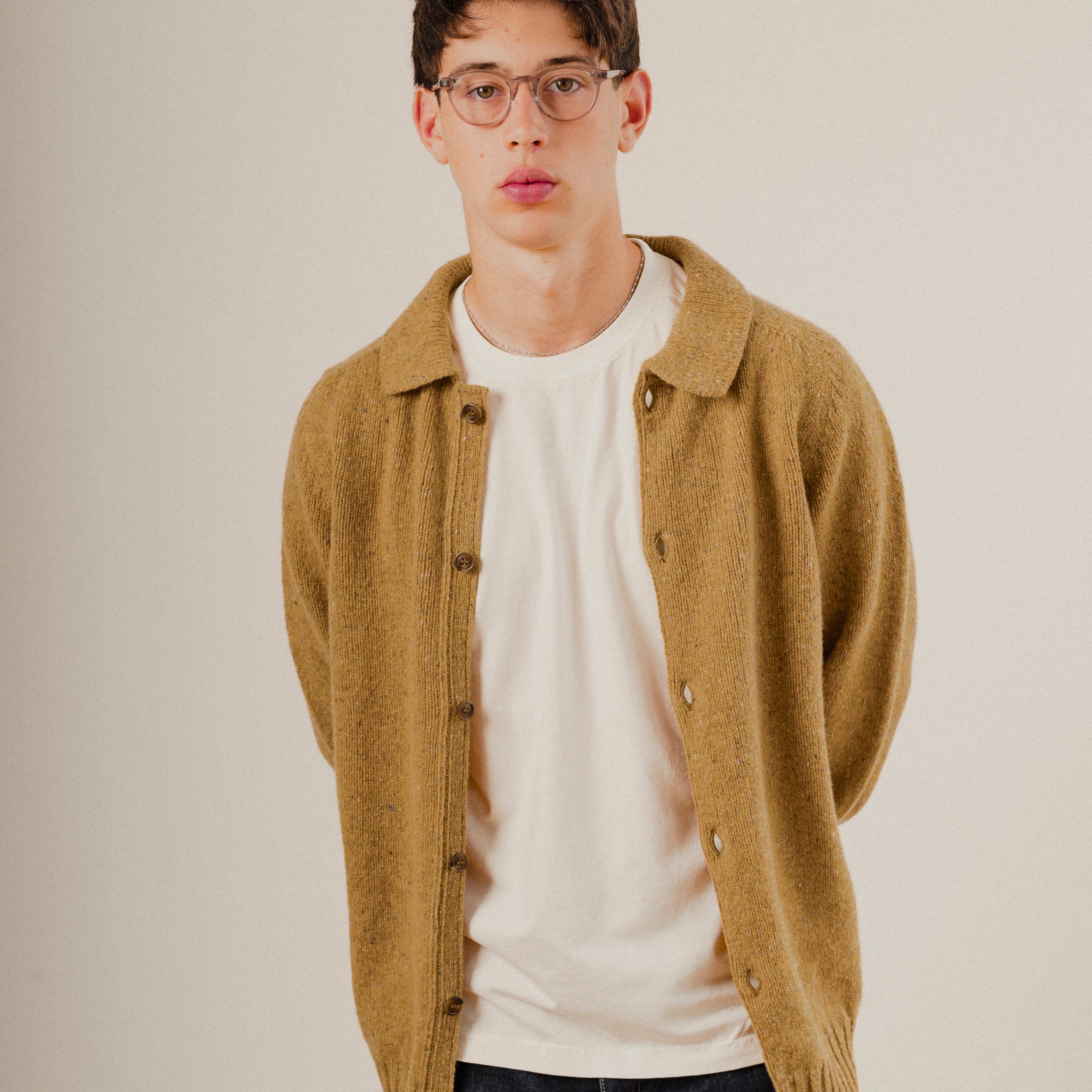 Man wearing a mustard yellow wool cardigan over a white shirt on a plain background