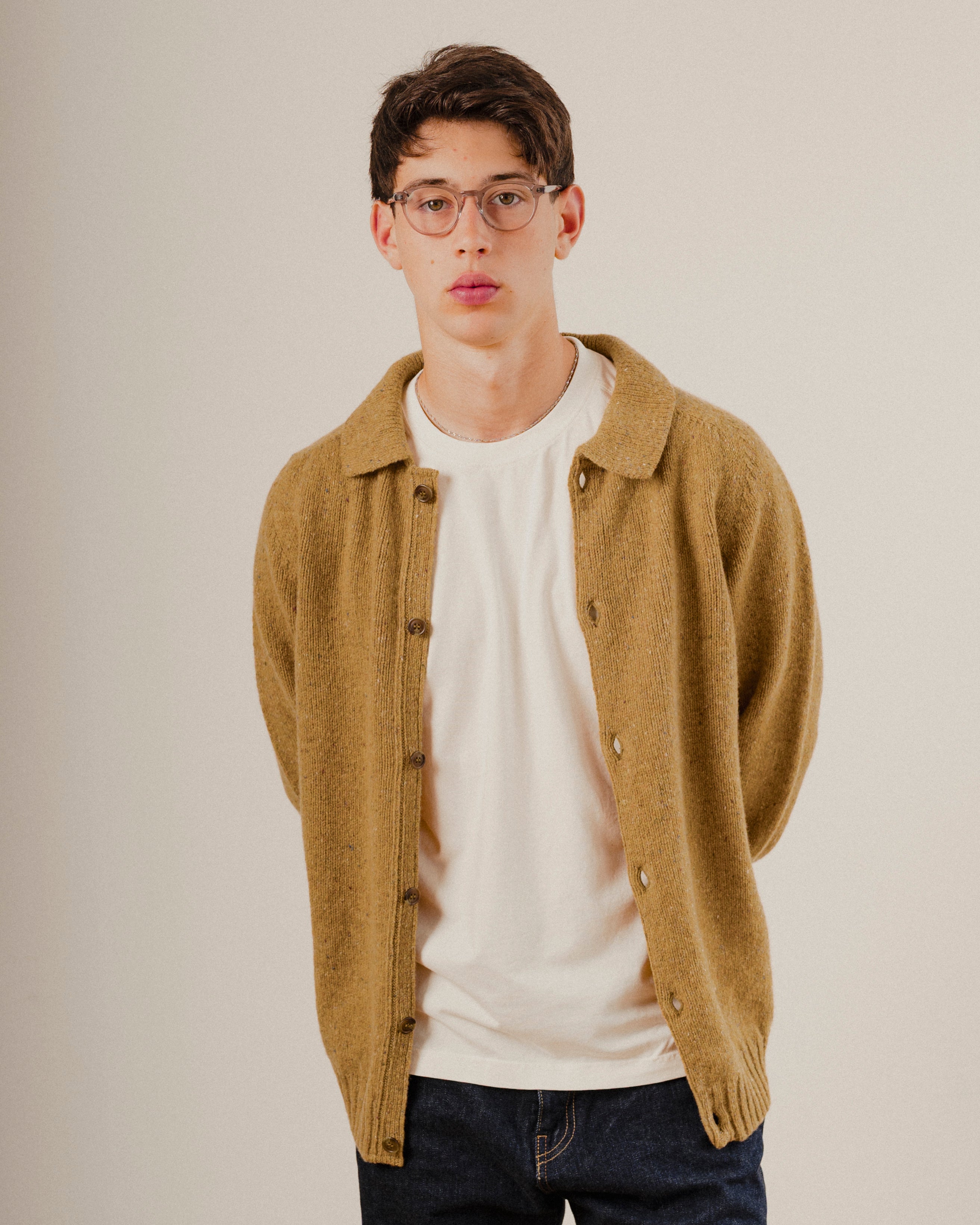 Man wearing a mustard yellow wool cardigan over a white shirt on a plain background