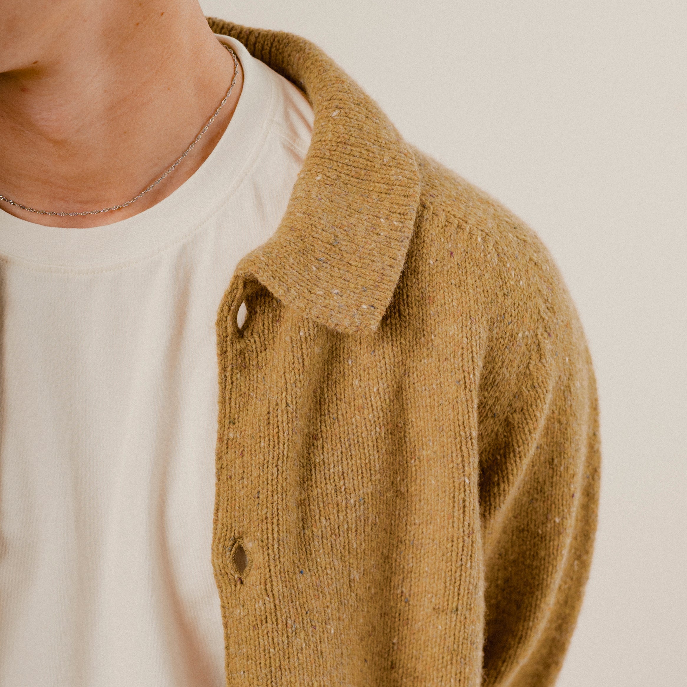 Close-up of a person wearing a mustard yellow knitted wool cardigan over a white shirt.