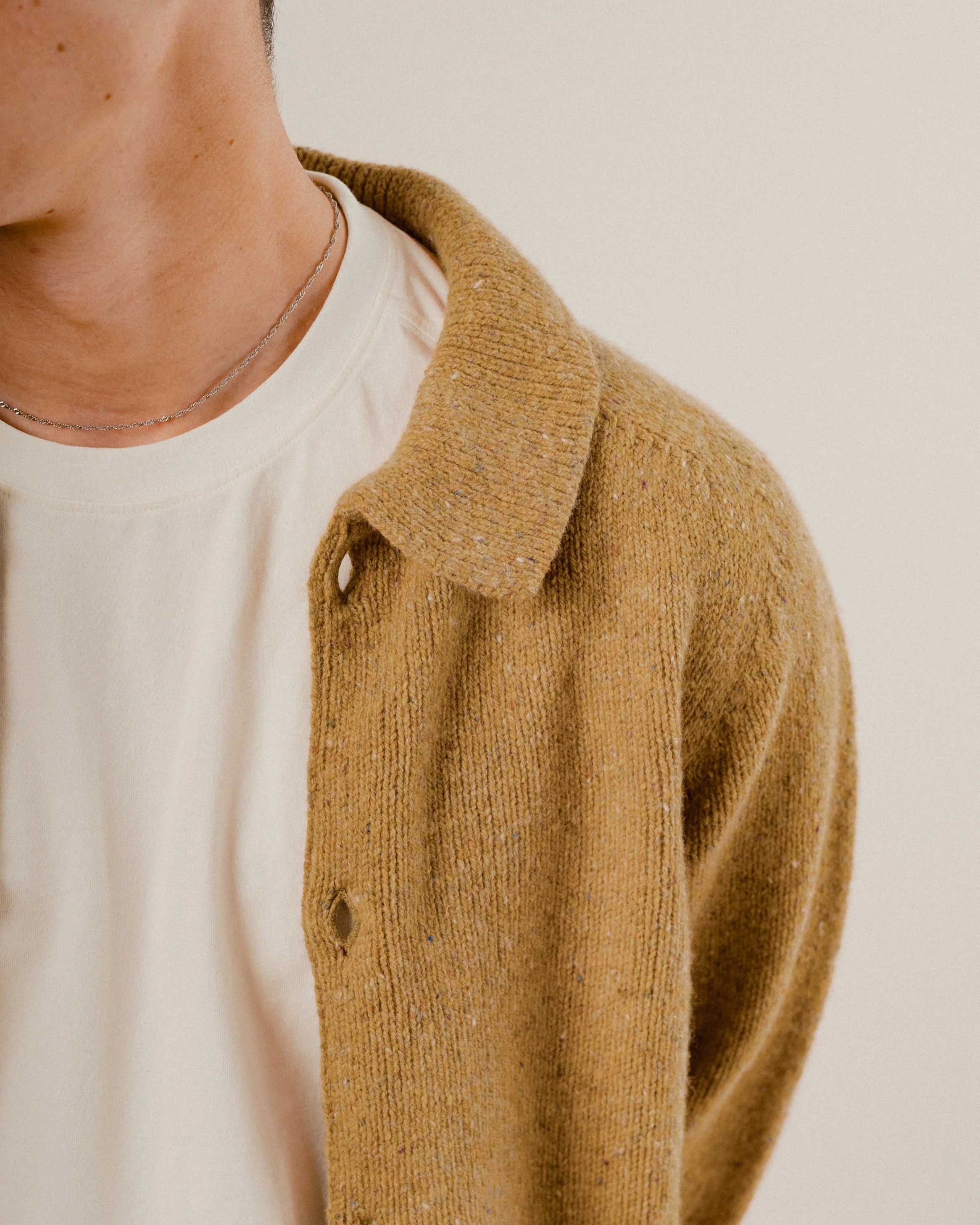 Close-up of a person wearing a mustard yellow knitted wool cardigan over a white shirt.