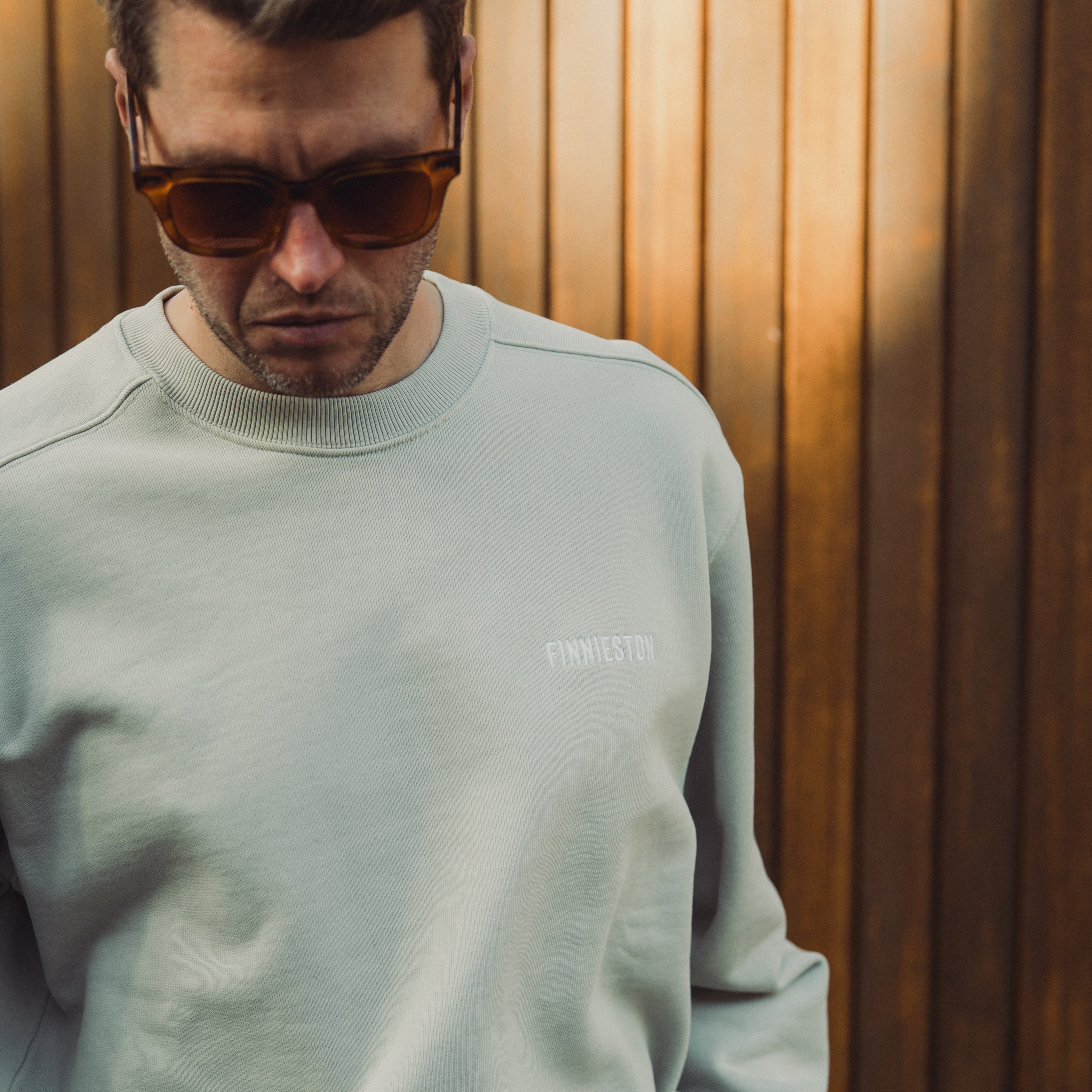 Man wearing a light gray sweatshirt with a logo against a wooden background