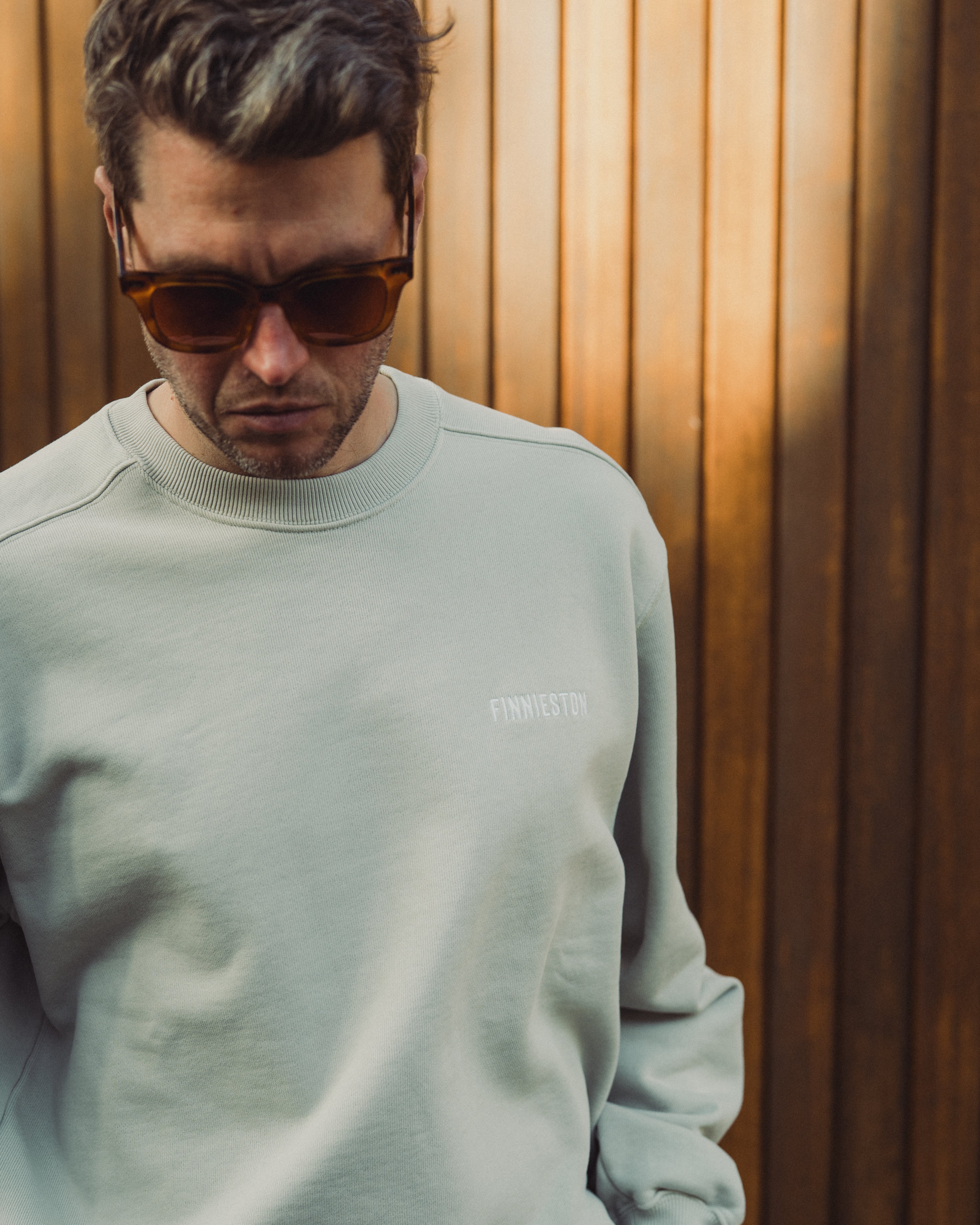 Man wearing a light gray sweatshirt with a logo against a wooden background