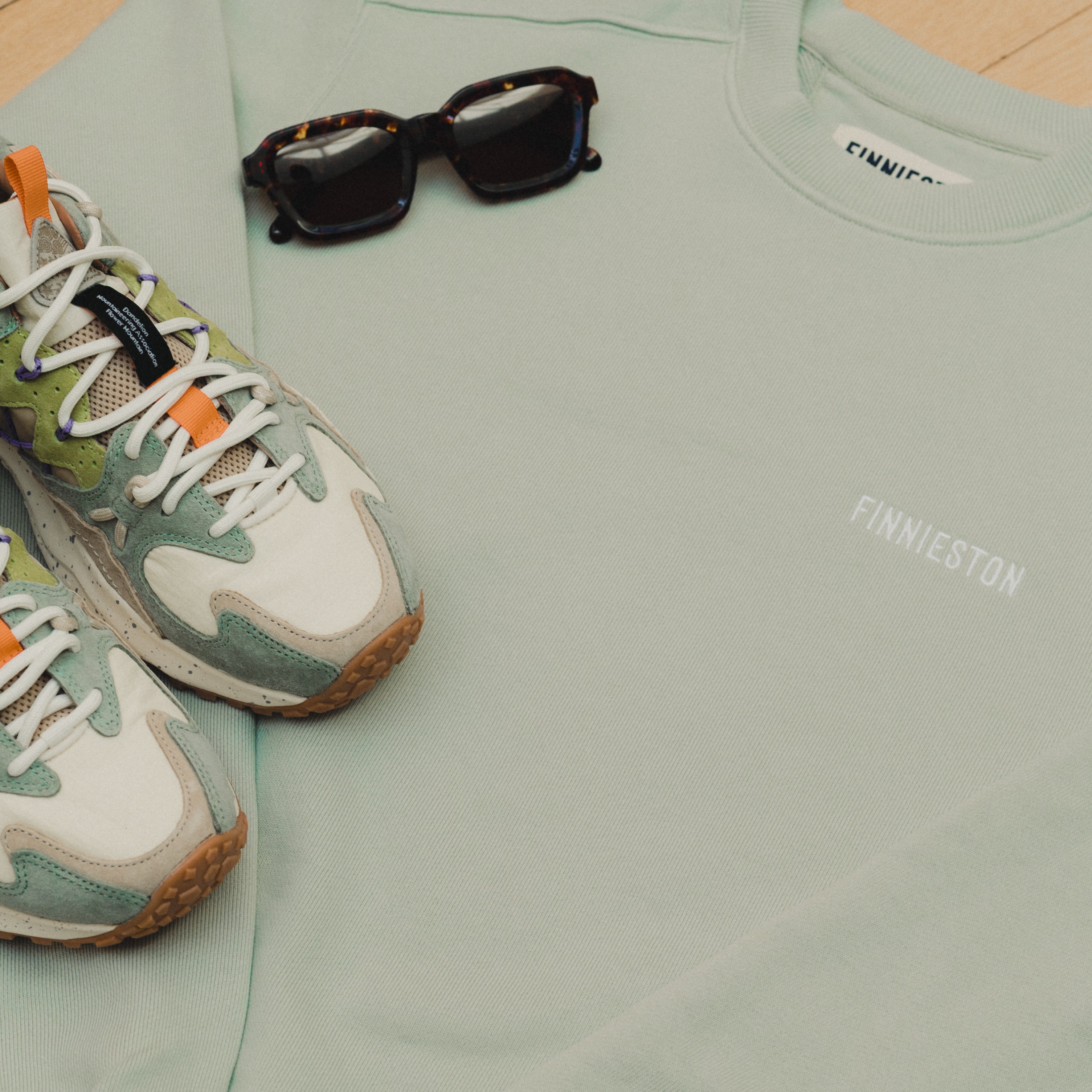 Light green sweatshirt with sunglasses and sneakers on a wooden floor