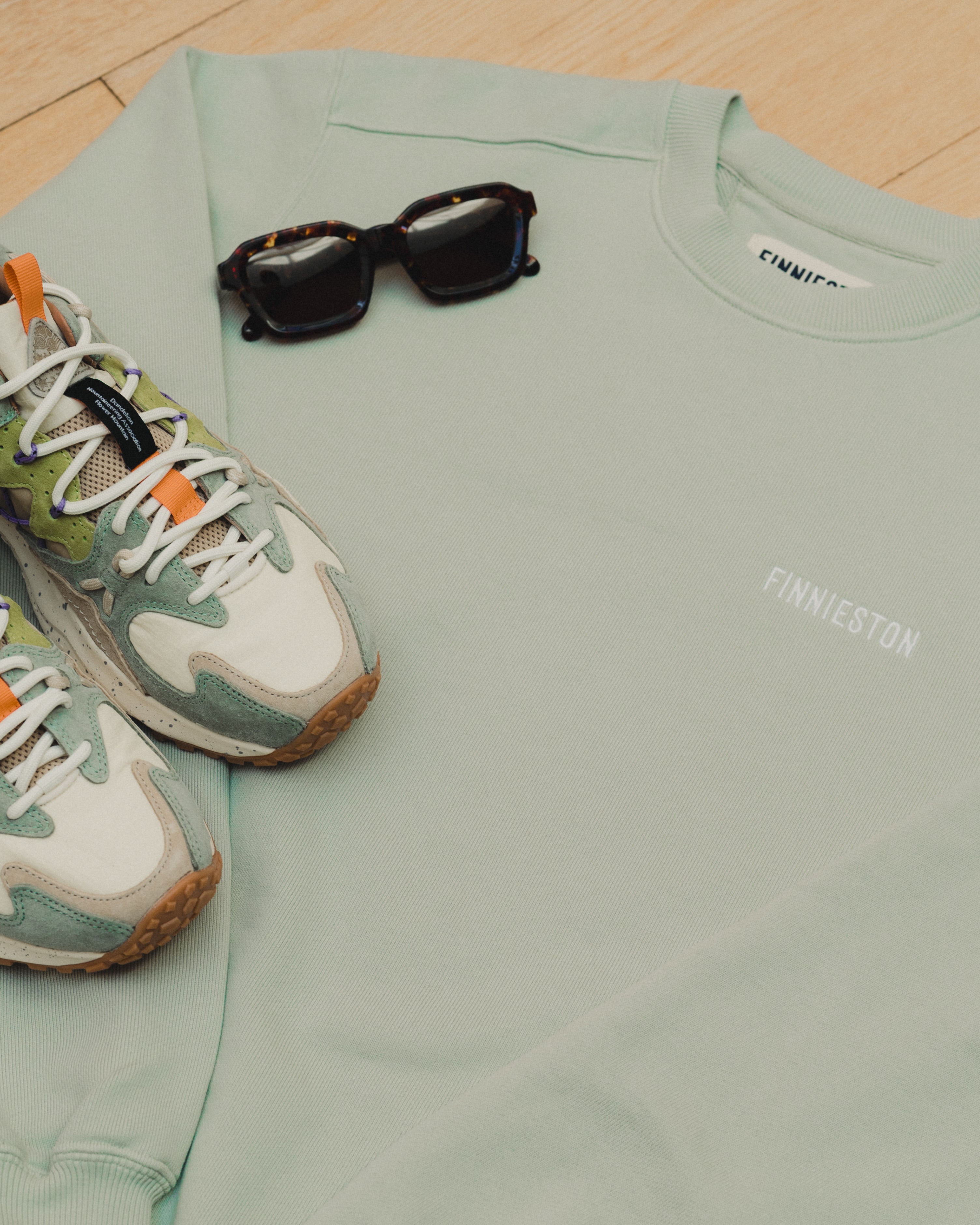 Light green sweatshirt with sunglasses and sneakers on a wooden floor