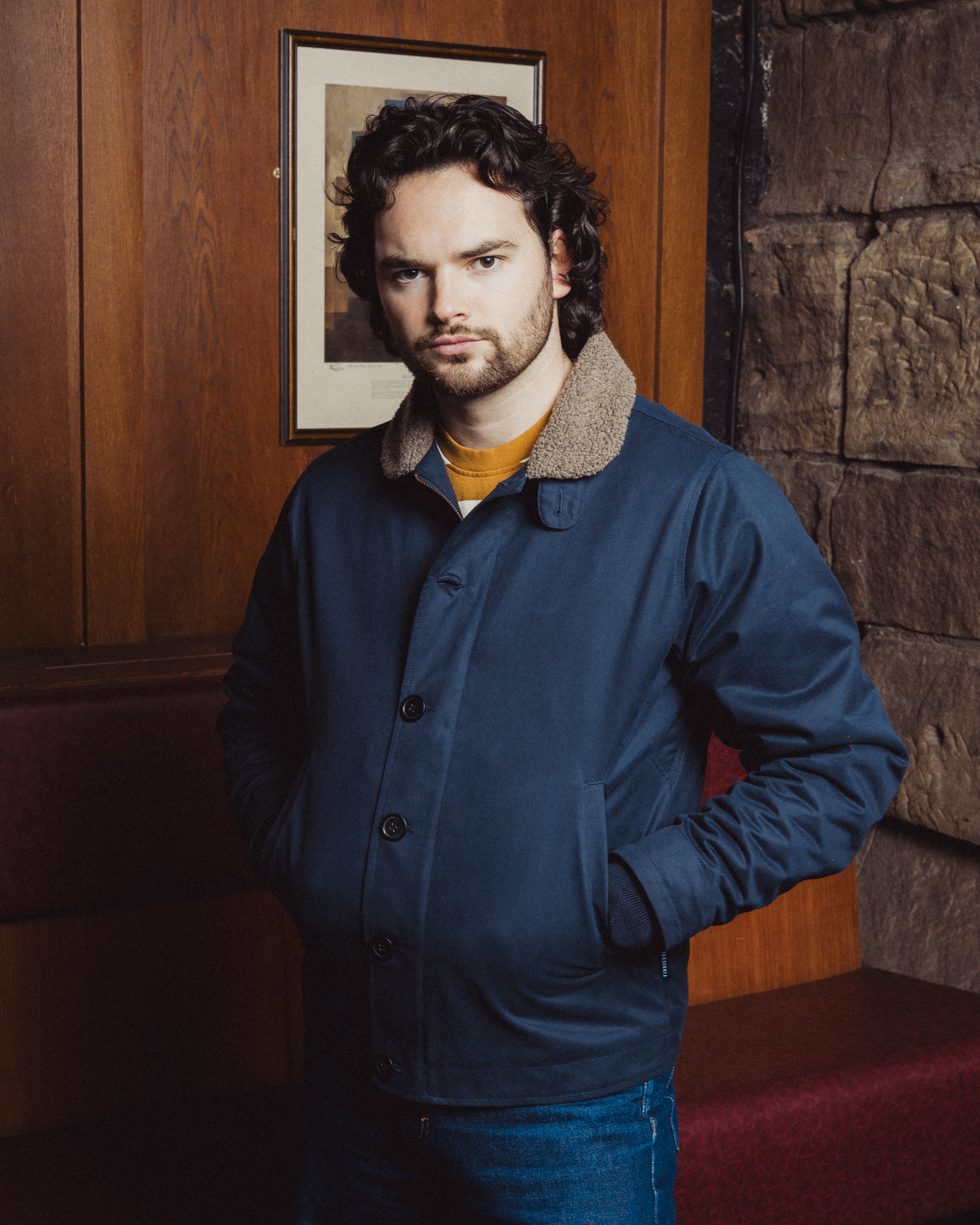 Man wearing a blue jacket in a room with wooden paneling and a stone wall.