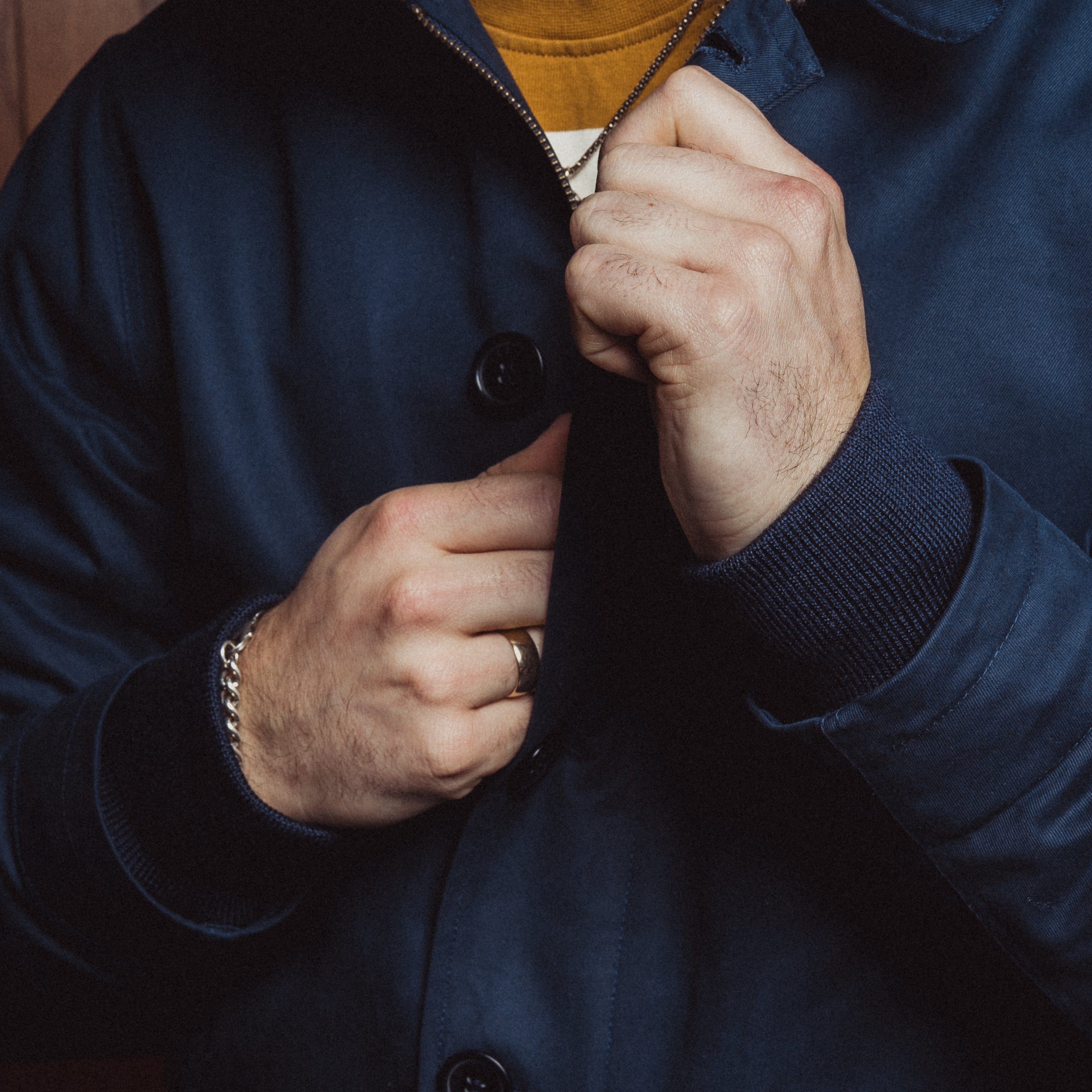 Person wearing a blue coat with a close-up of hands buttoning it up.