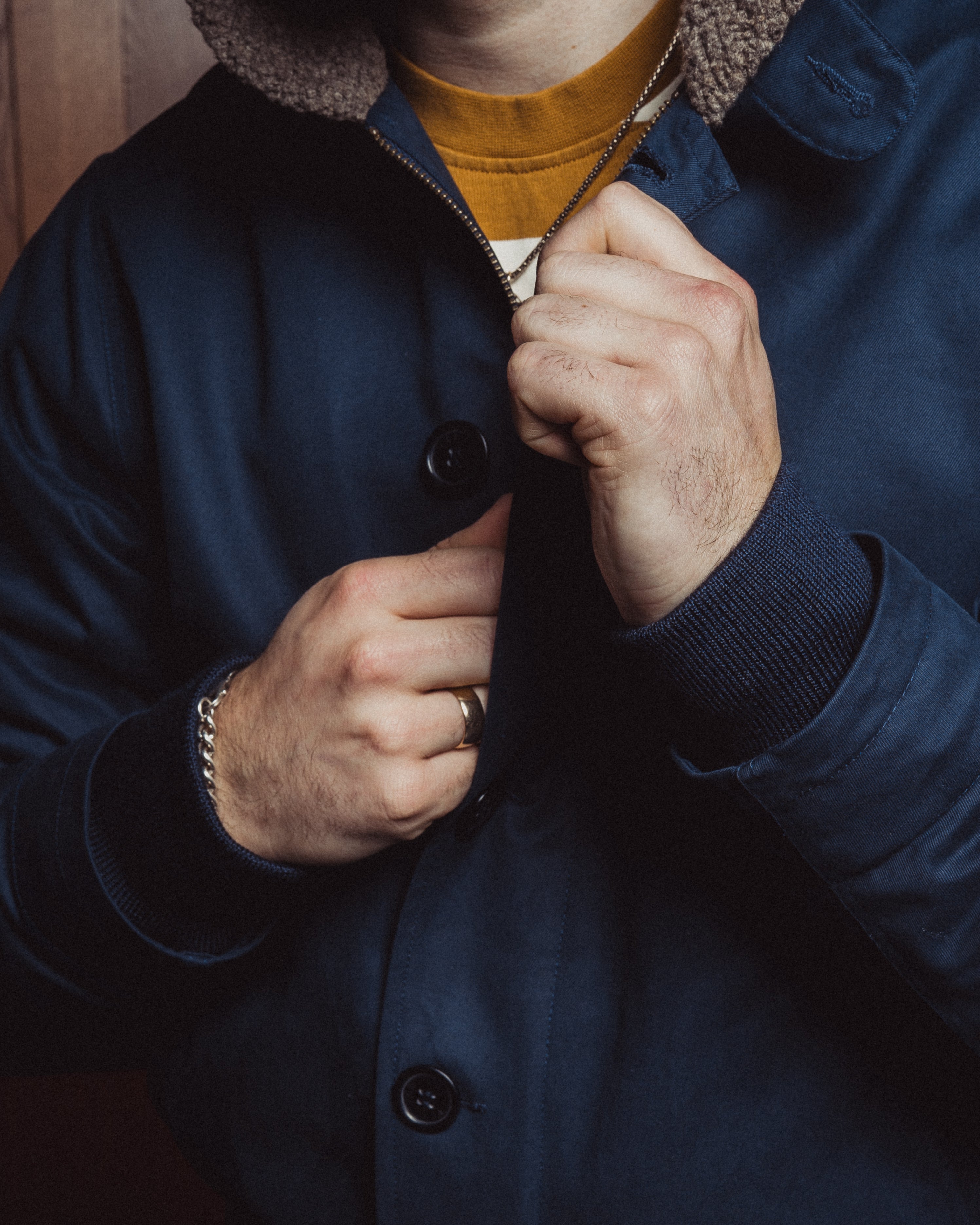 Person wearing a blue coat with a close-up of hands buttoning it up.