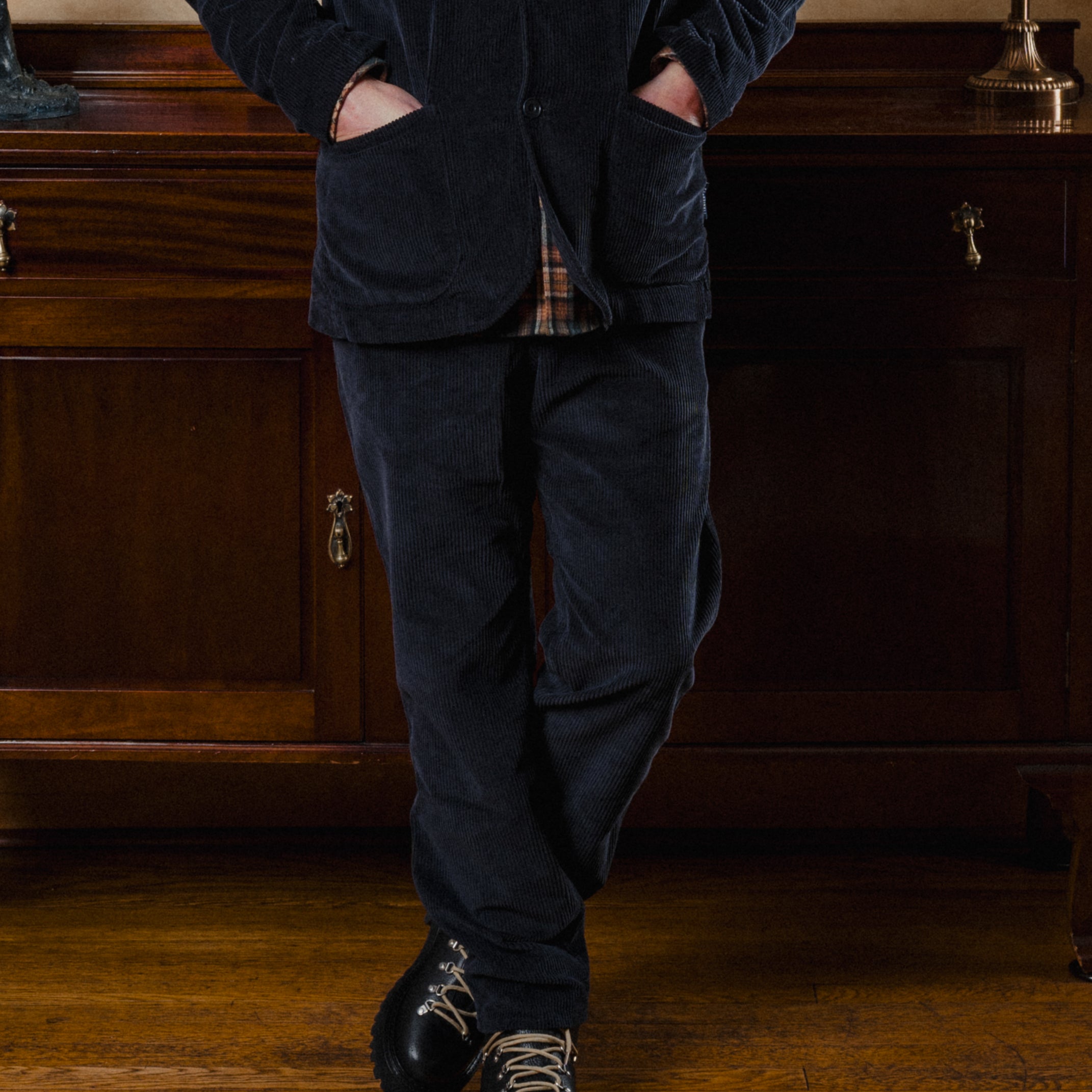 Person wearing a dark blue corduroy suit standing in a room with wooden furniture.