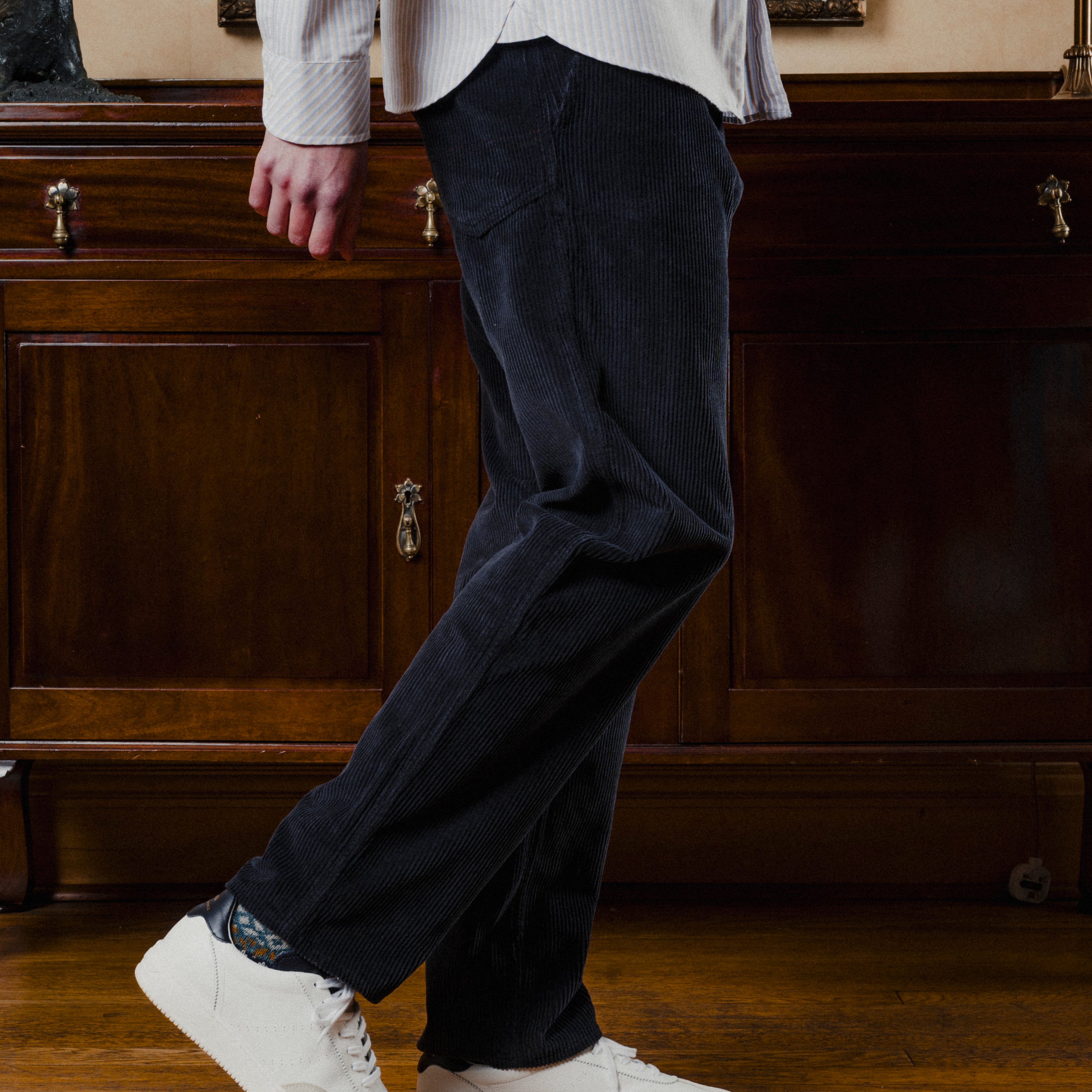 Person wearing dark pants and white sneakers in a room with wooden furniture.