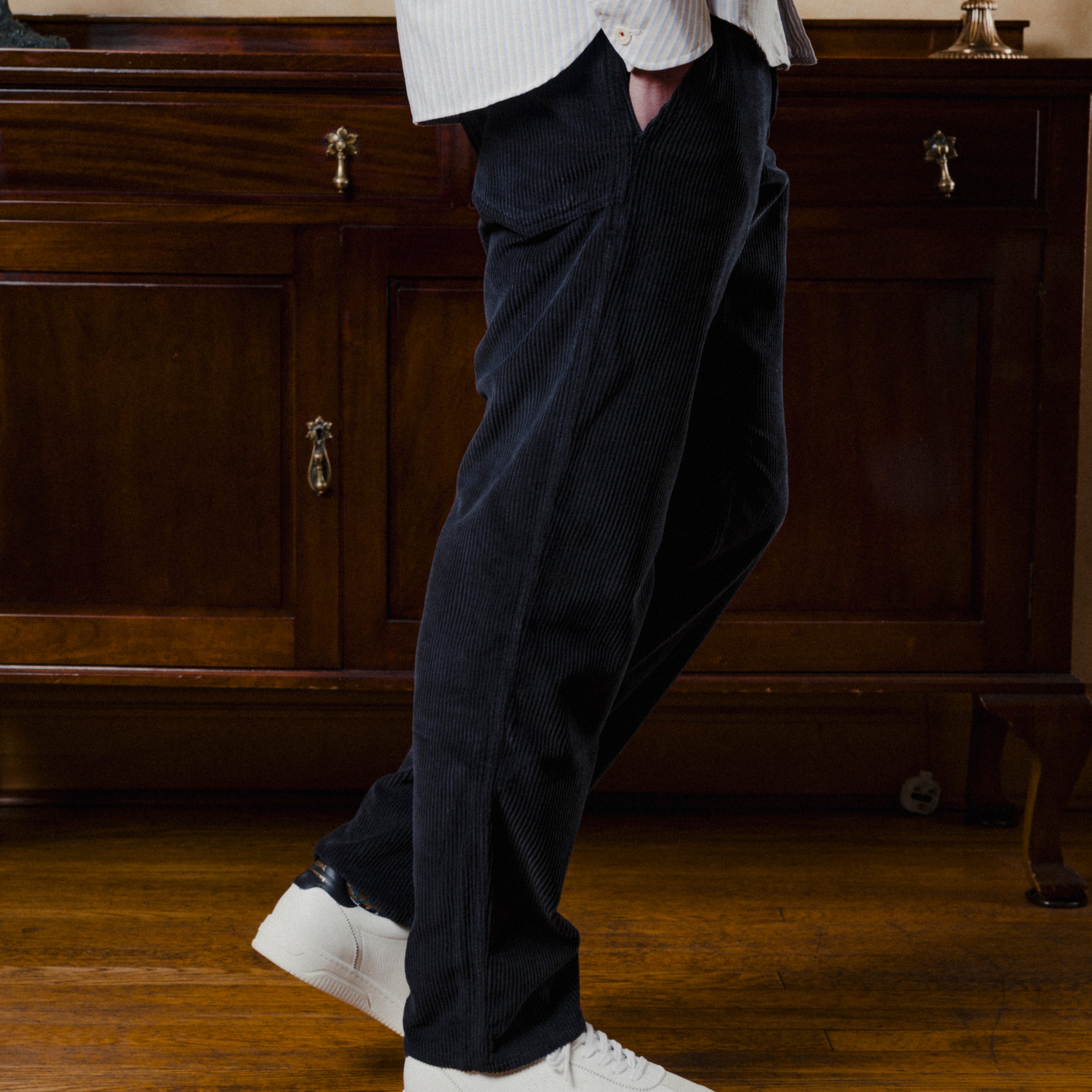 Person wearing dark pants and white sneakers in a room with wooden furniture.