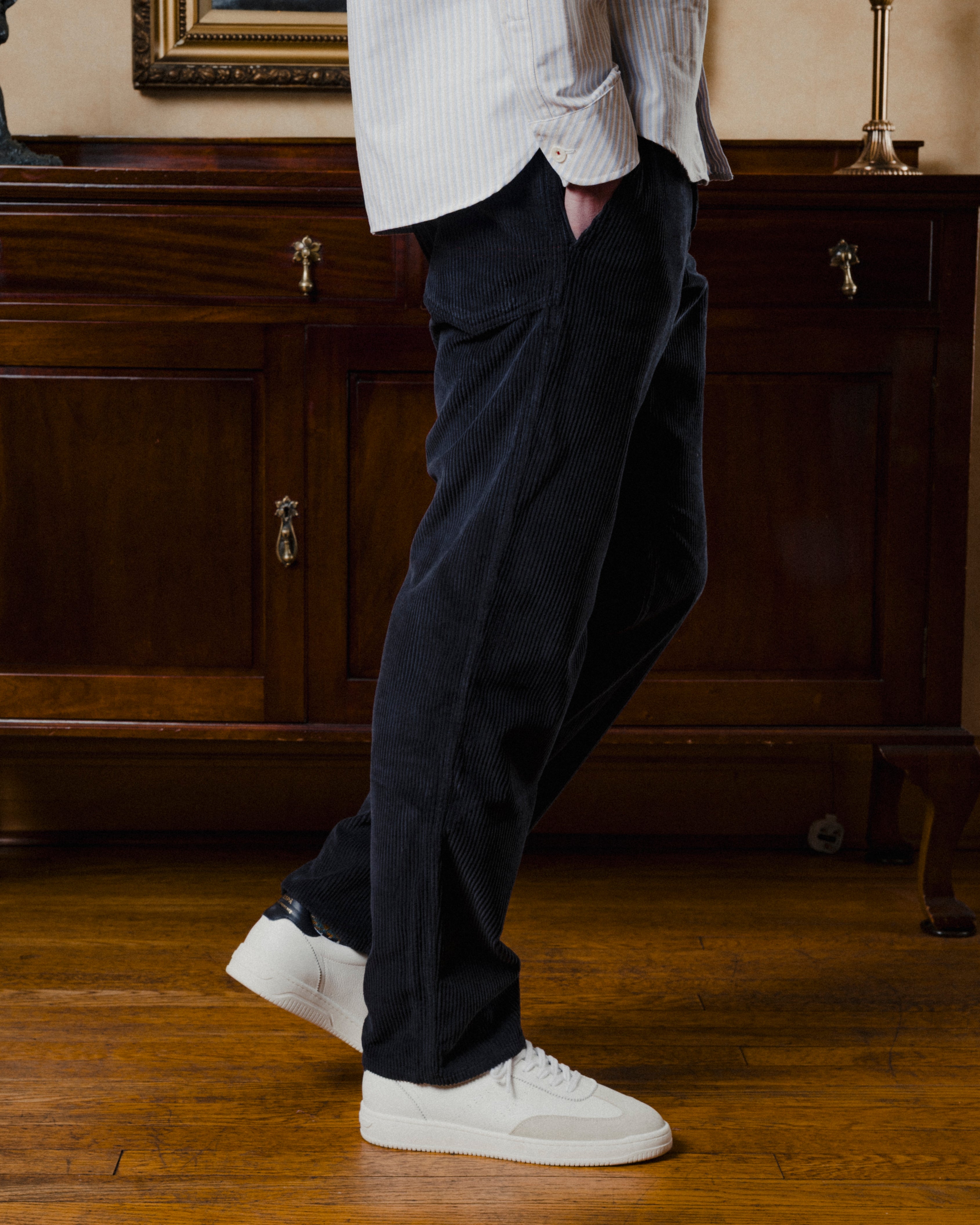 Person wearing dark pants and white sneakers in a room with wooden furniture.