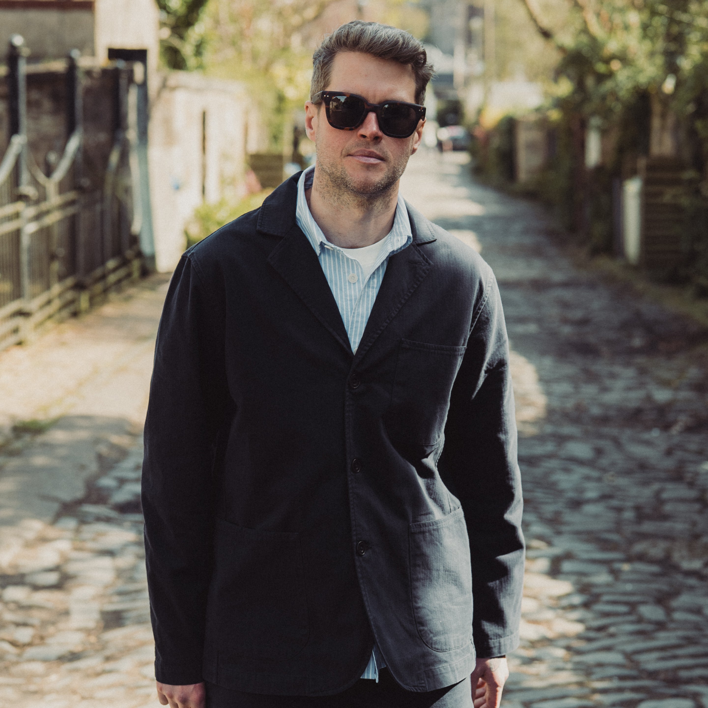 Man wearing sunglasses and a dark jacket on a cobblestone street