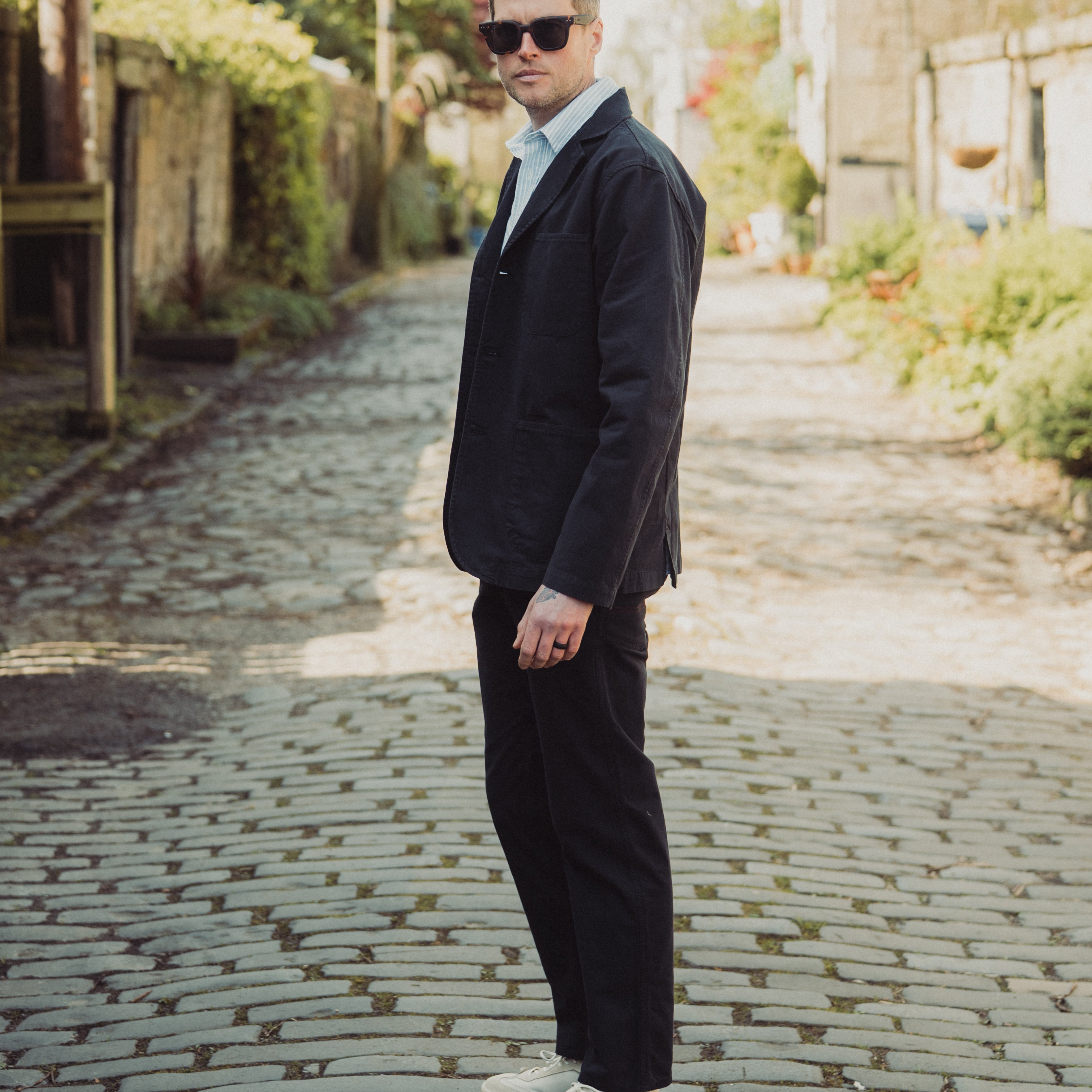 Man in a dark suit and sunglasses standing on a cobblestone street.