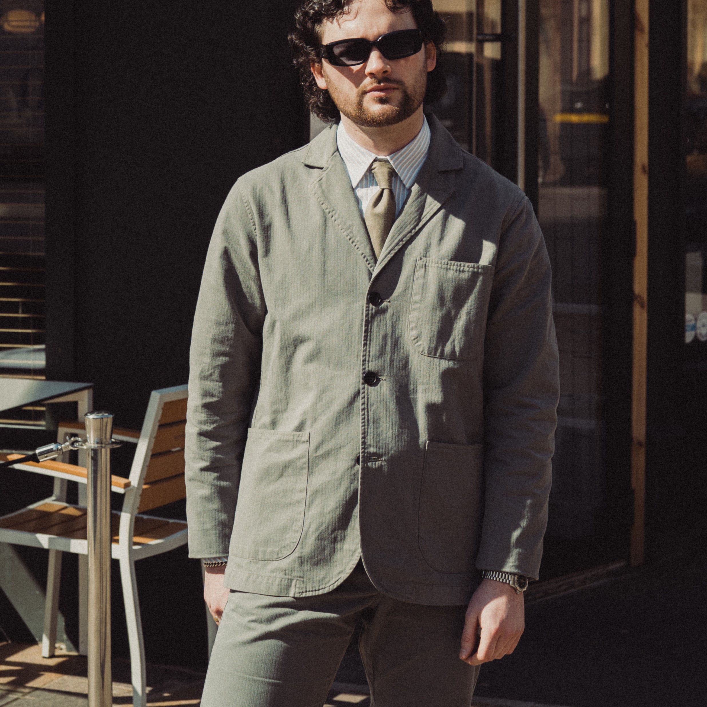 Man wearing a green jacket and brown pants standing outdoors.