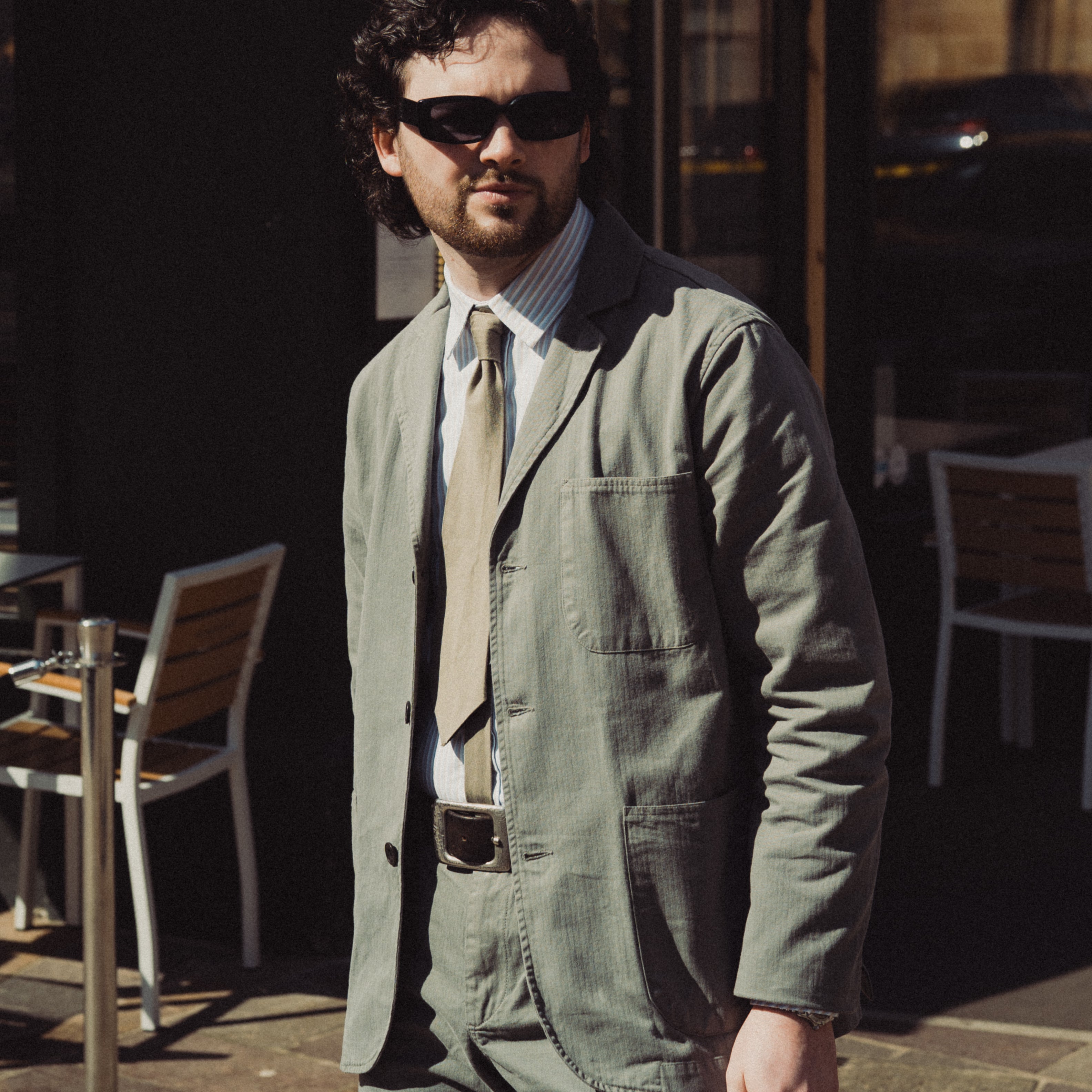 Man wearing sunglasses and a green jacket standing outdoors.