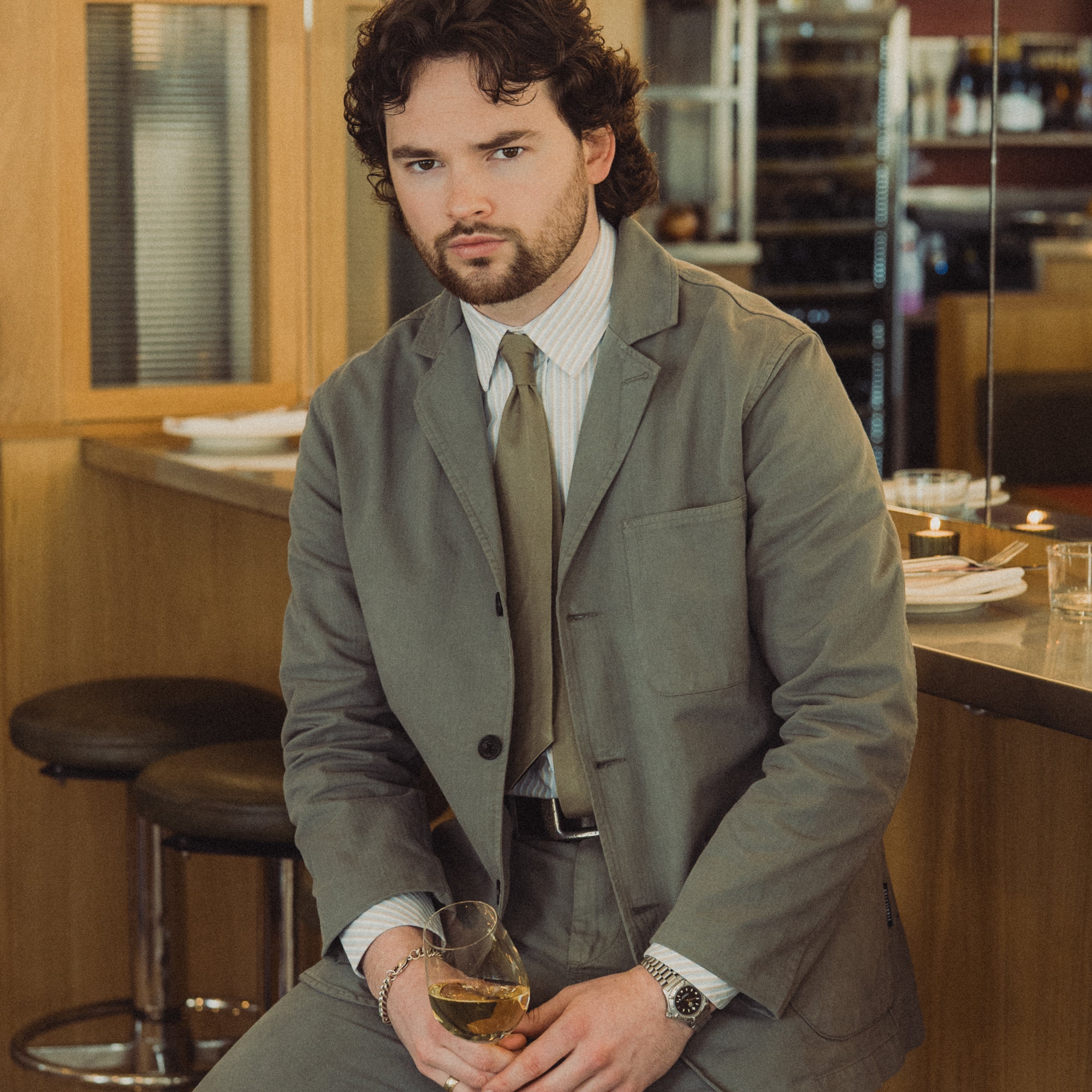 Man in a gray suit sitting at a bar holding a drink