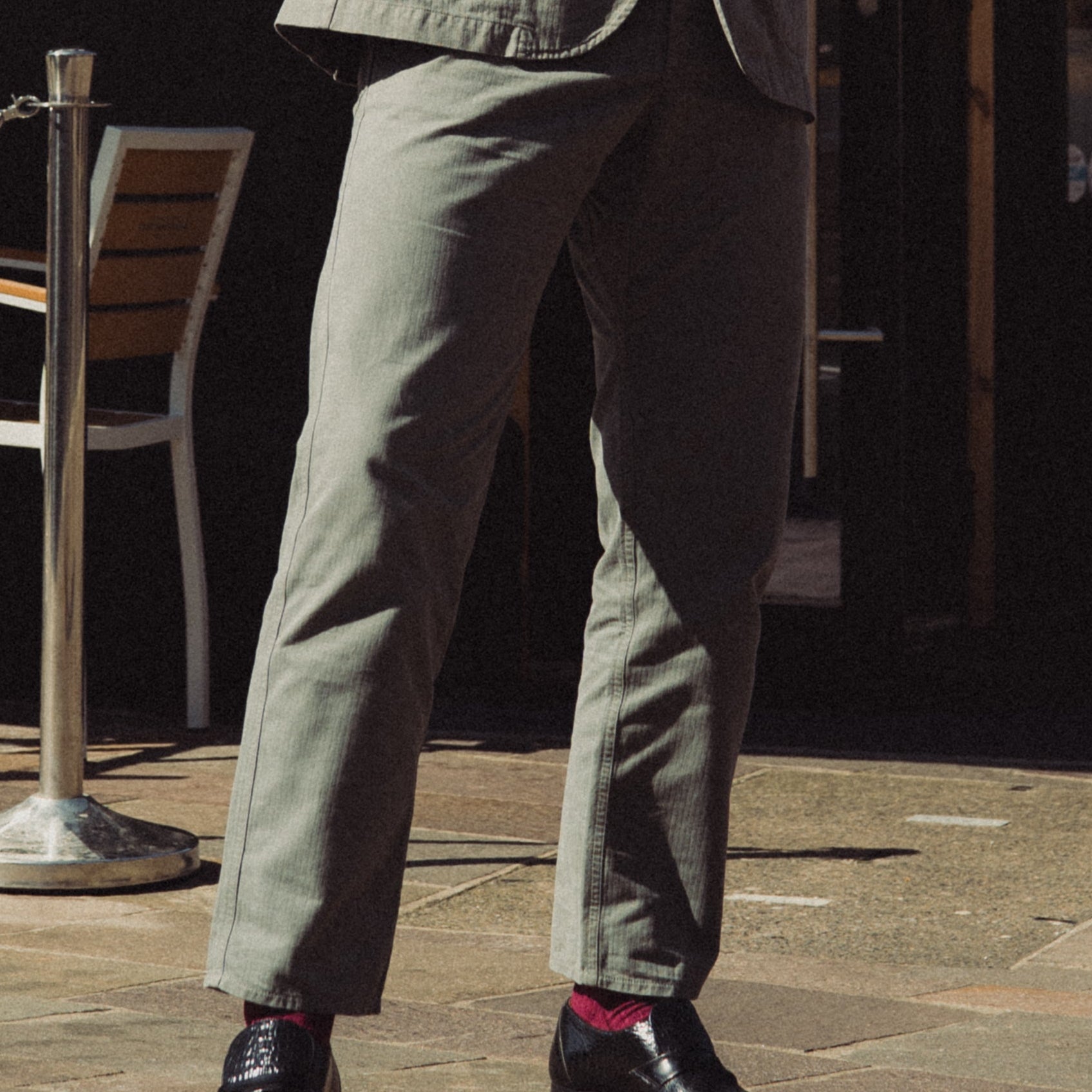 Man in a suit standing outside a corner shop with tables and chairs.