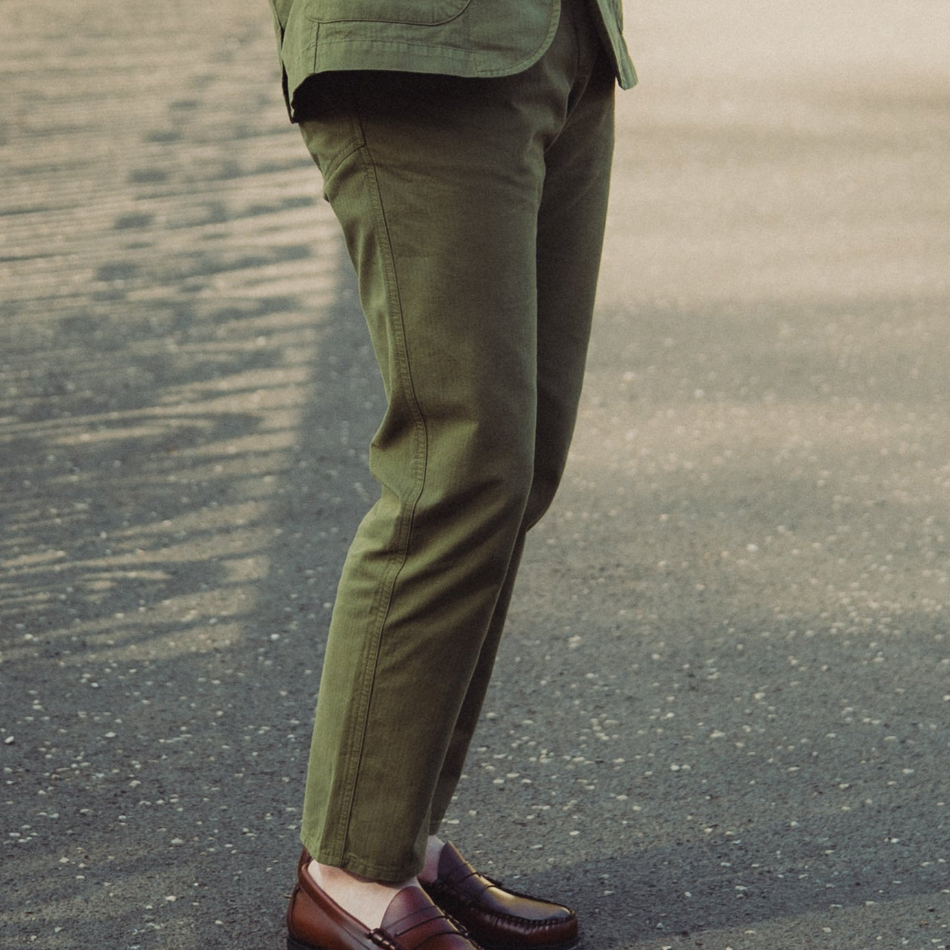 Man in a green suit standing on a pathway with white gates and greenery in the background