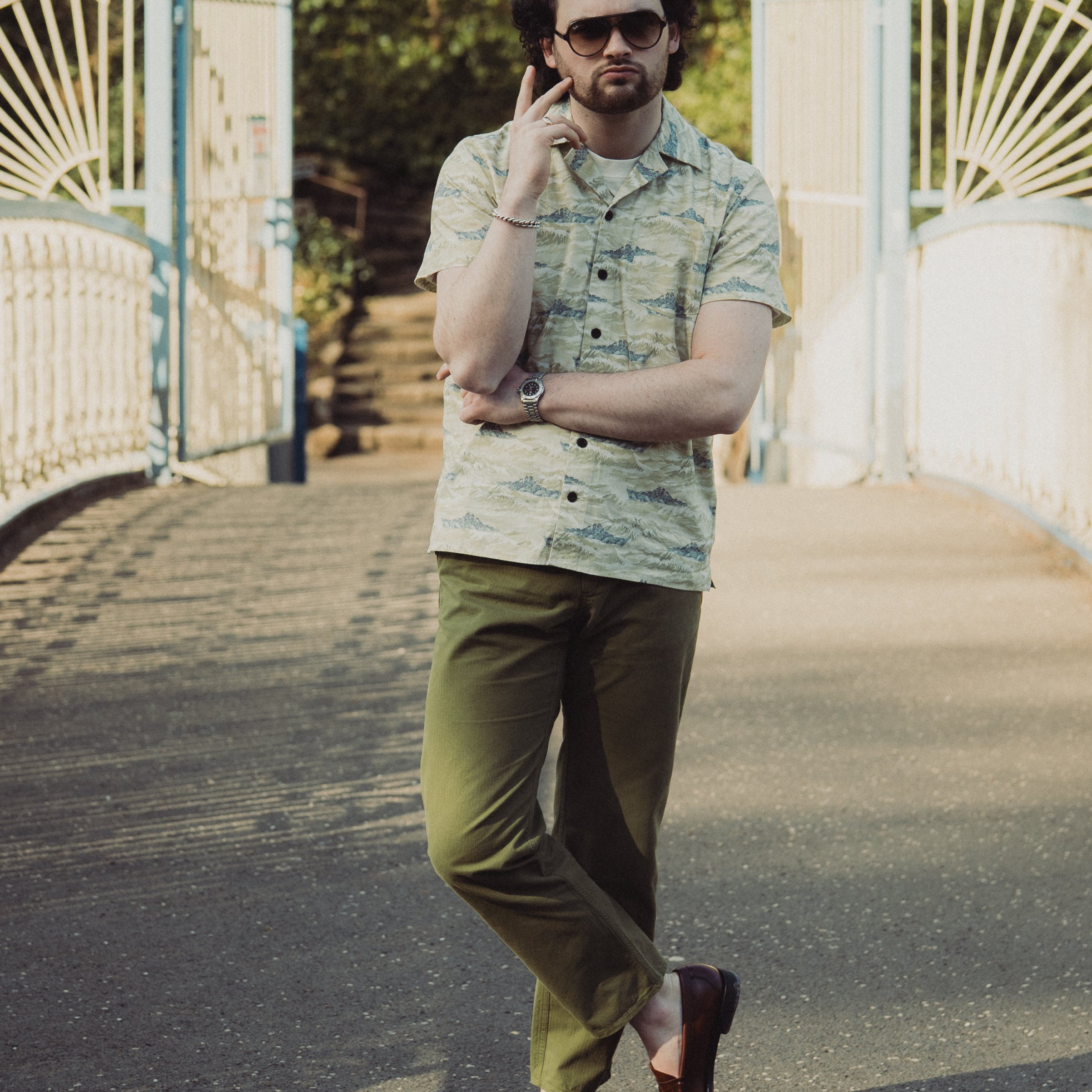 Man in a patterned shirt and green pants standing on a bridge