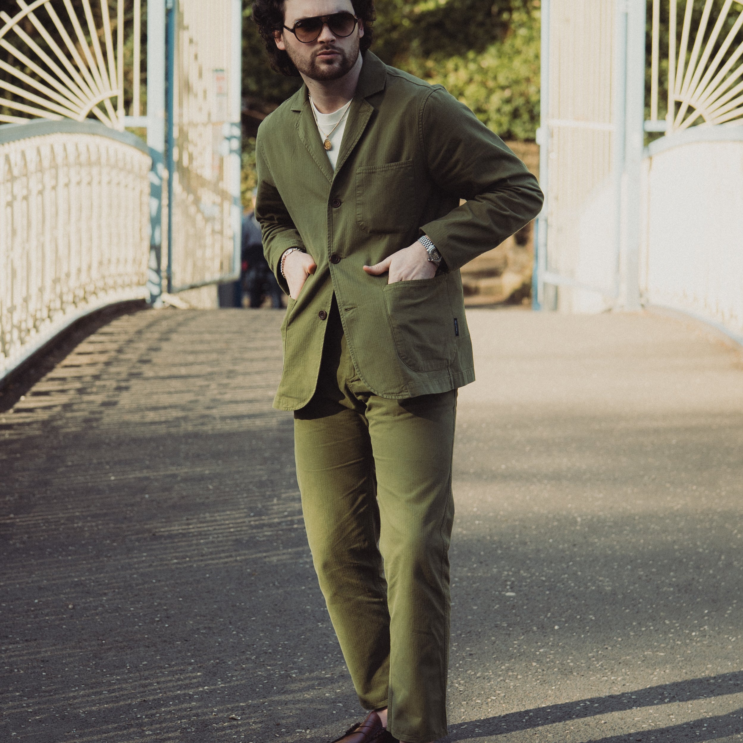 Man in a green suit standing on a bridge with white railings.