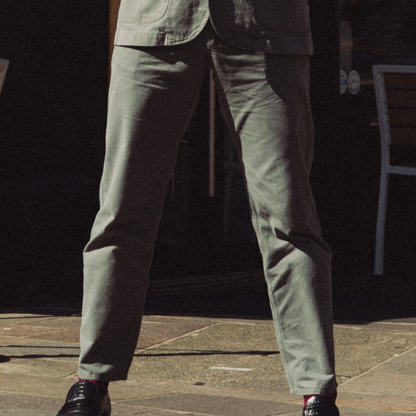 Man in a suit standing in front of a corner shop with outdoor seating.