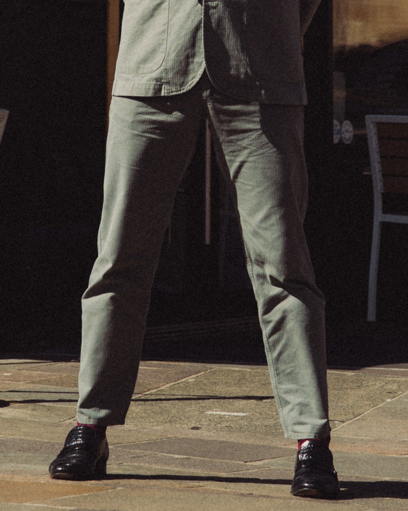 Man in a suit standing in front of a corner shop with outdoor seating.