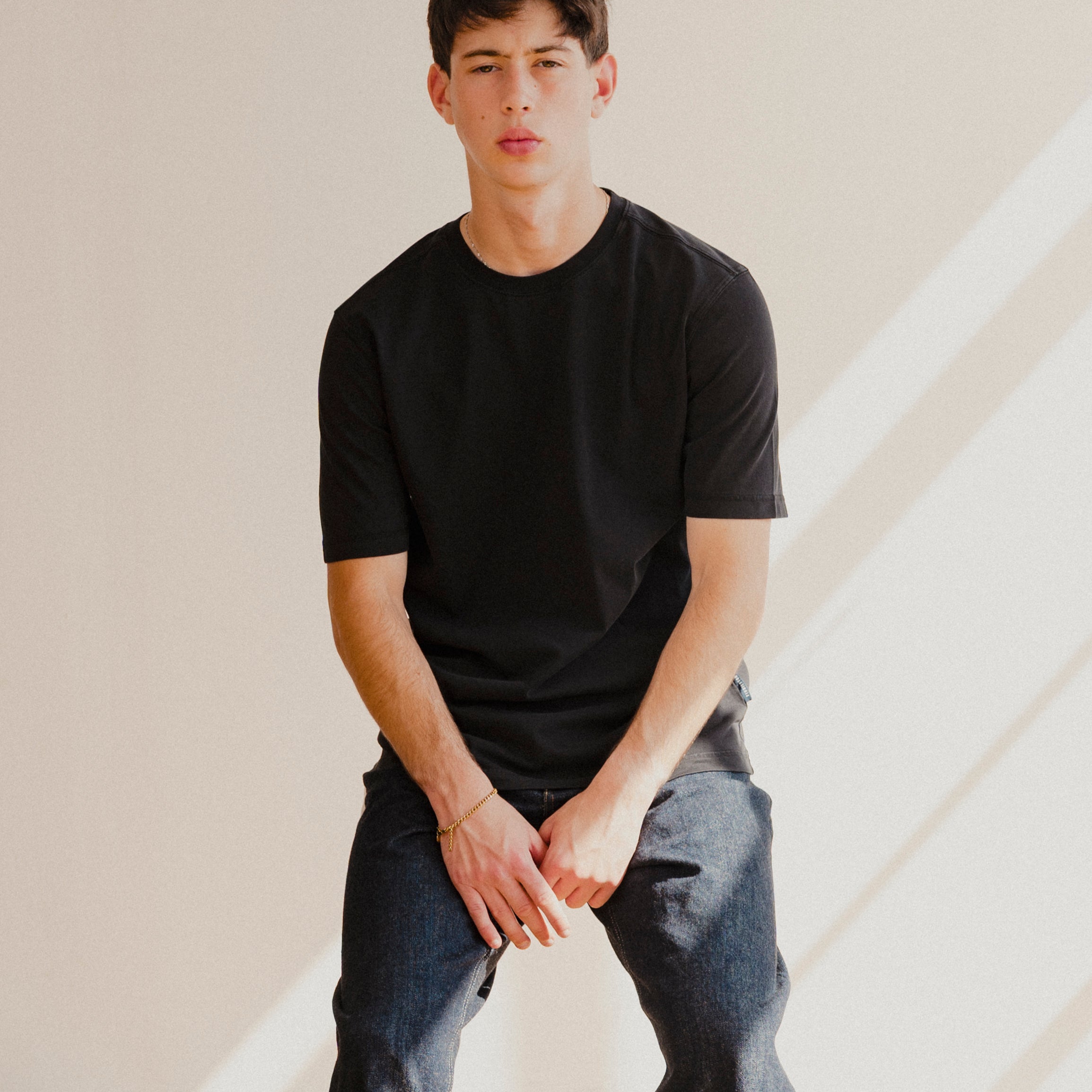 Person wearing a black t-shirt and gray pants sitting against a neutral background
