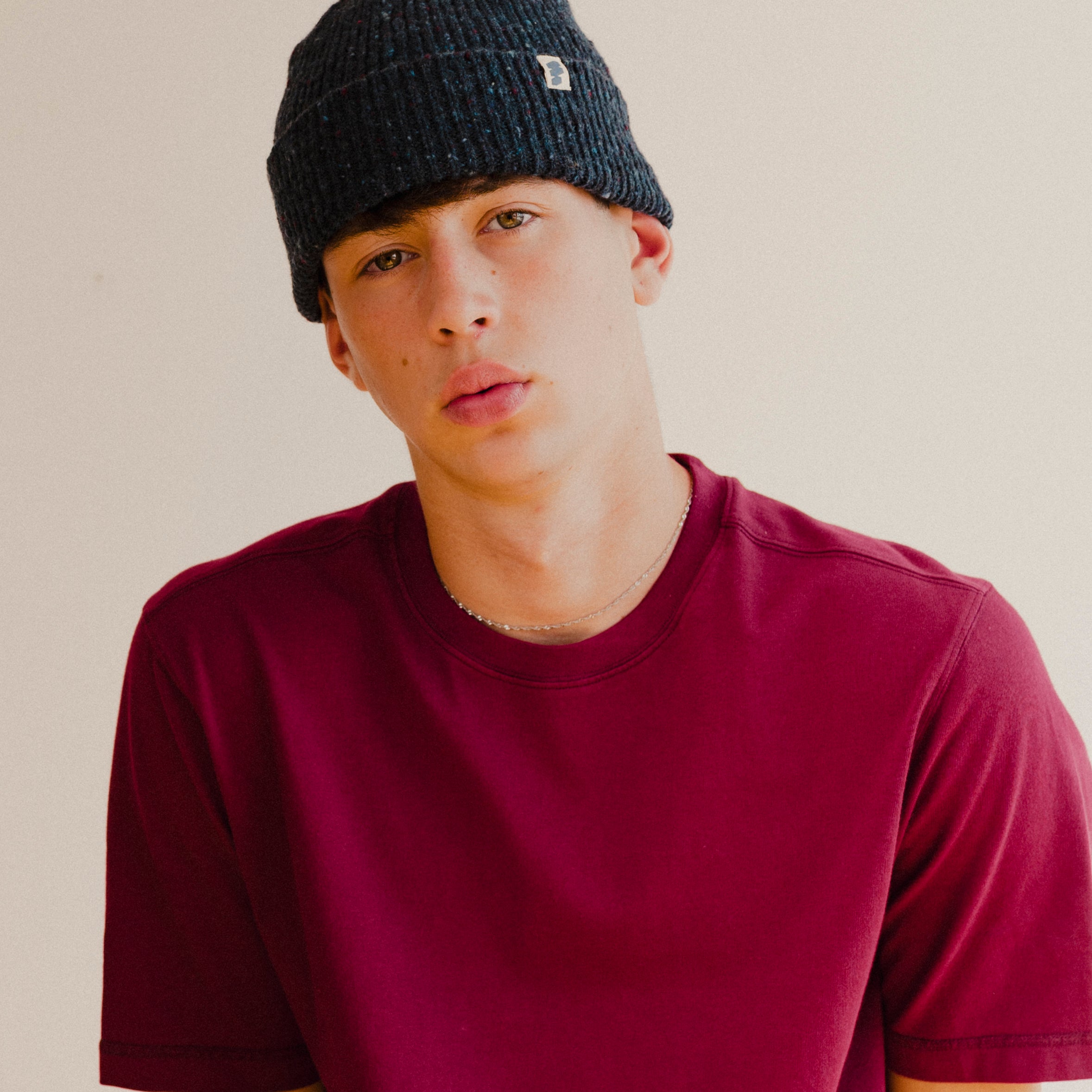 Person wearing a dark navy blue beanie and maroon red shirt against a plain background