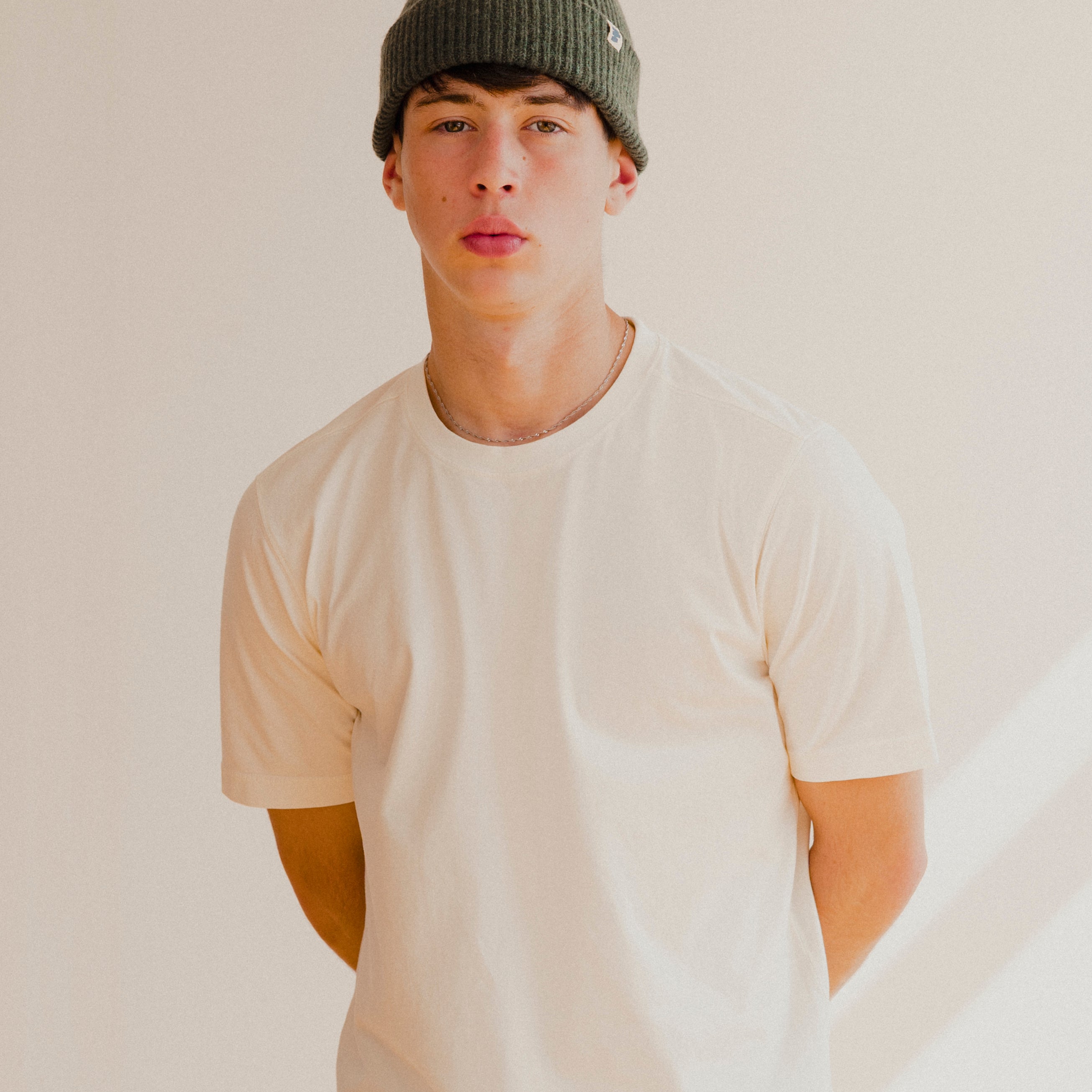 Person wearing a white t-shirt and green beanie against a plain background