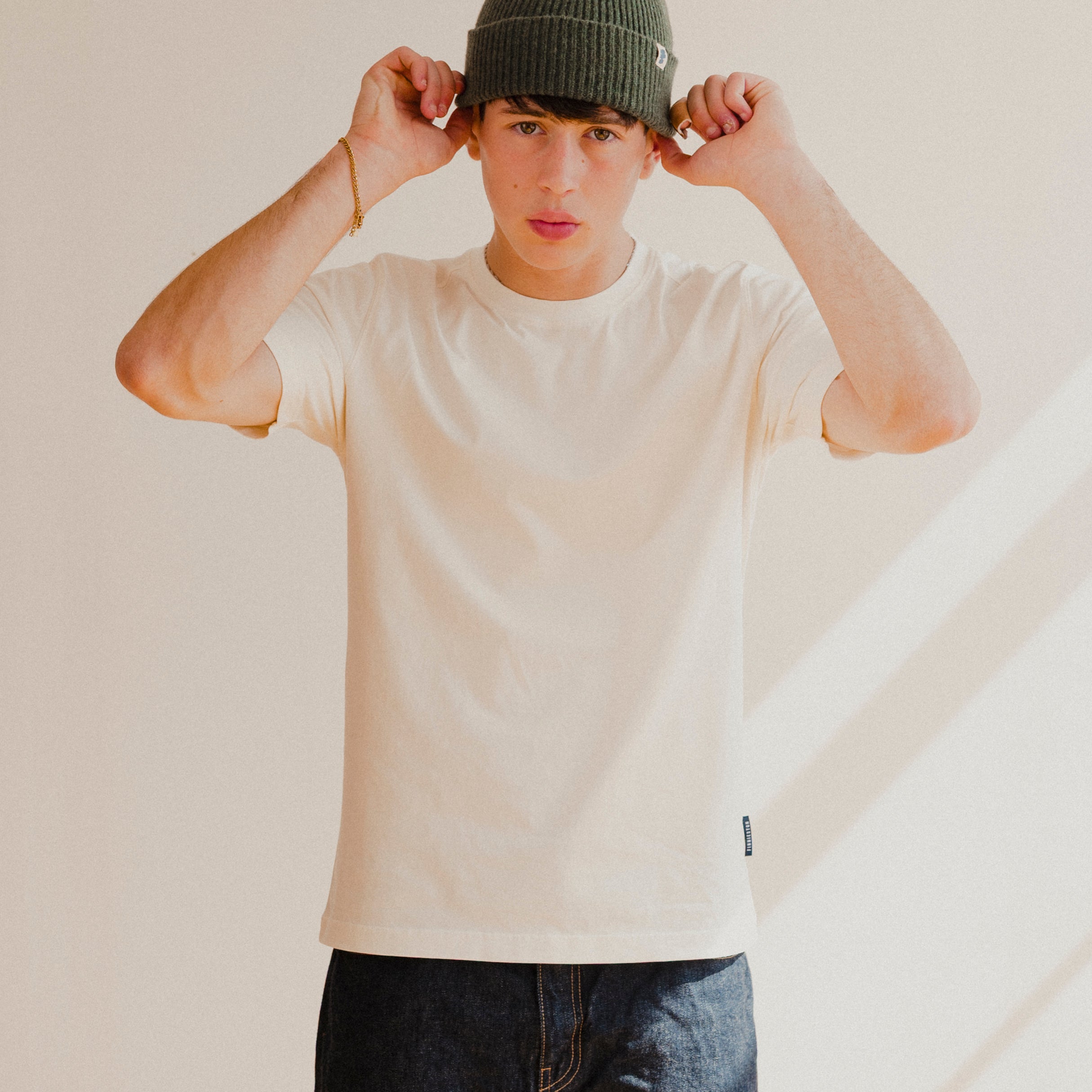 Person wearing a white t-shirt and dark jeans with a plain background