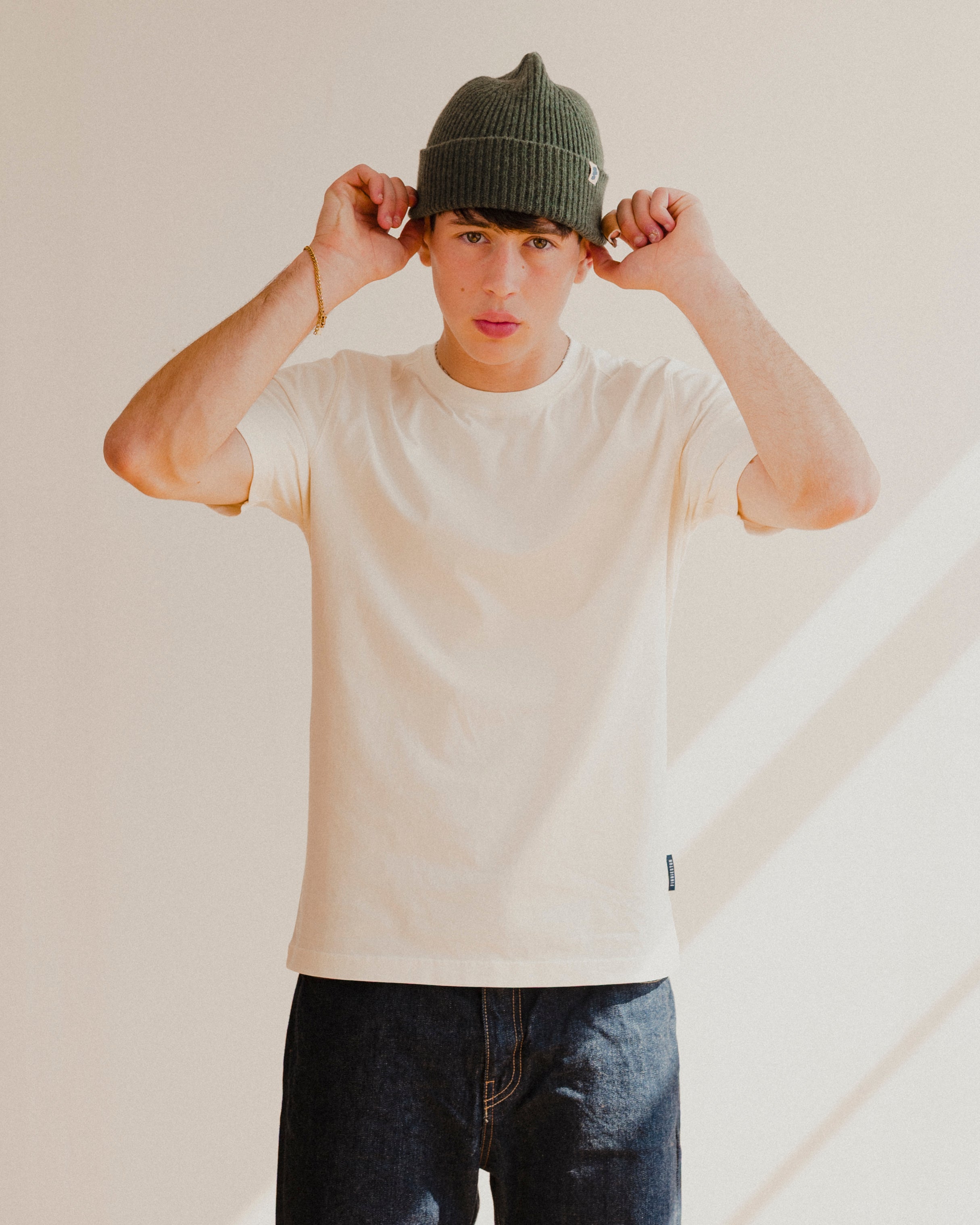 Person wearing a white t-shirt and dark jeans with a plain background